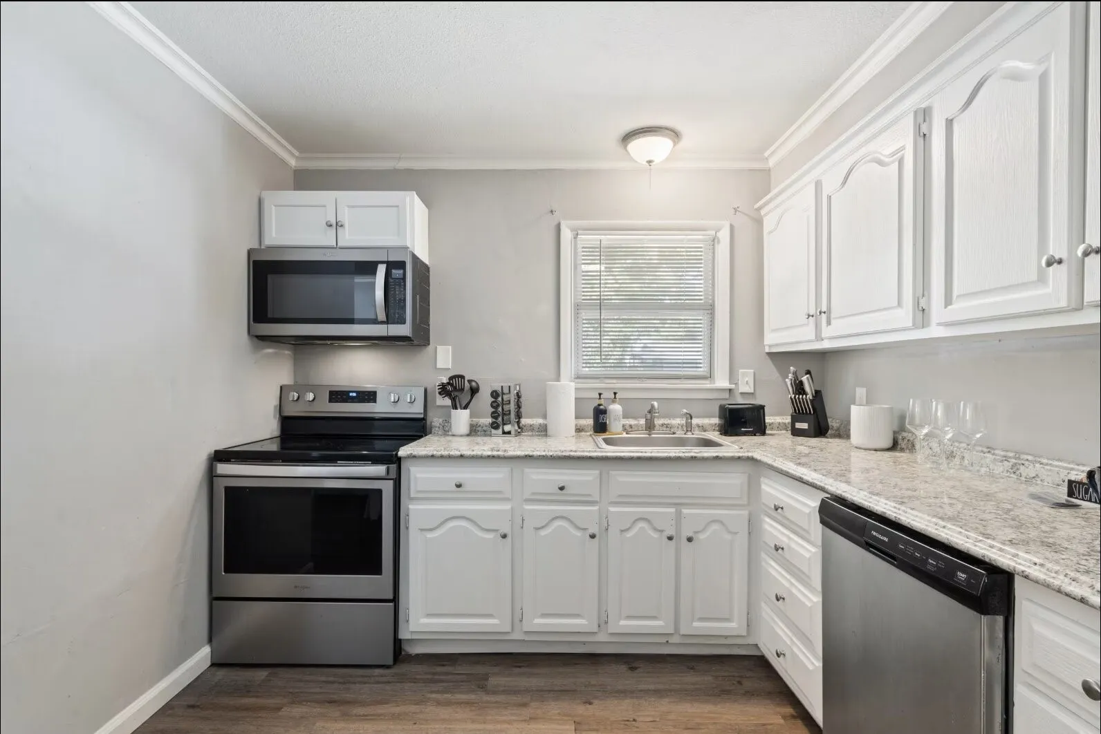 Kitchen featuring white cabinetry, light-toned countertops, stainless steel appliances, and wood-finish flooring