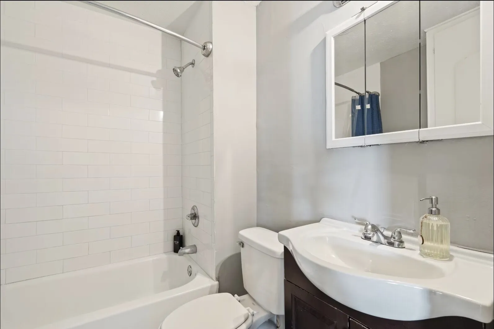 Bathtub with subway tile surround, chrome fixtures, vanity with integrated sink, and mirrored medicine cabinet