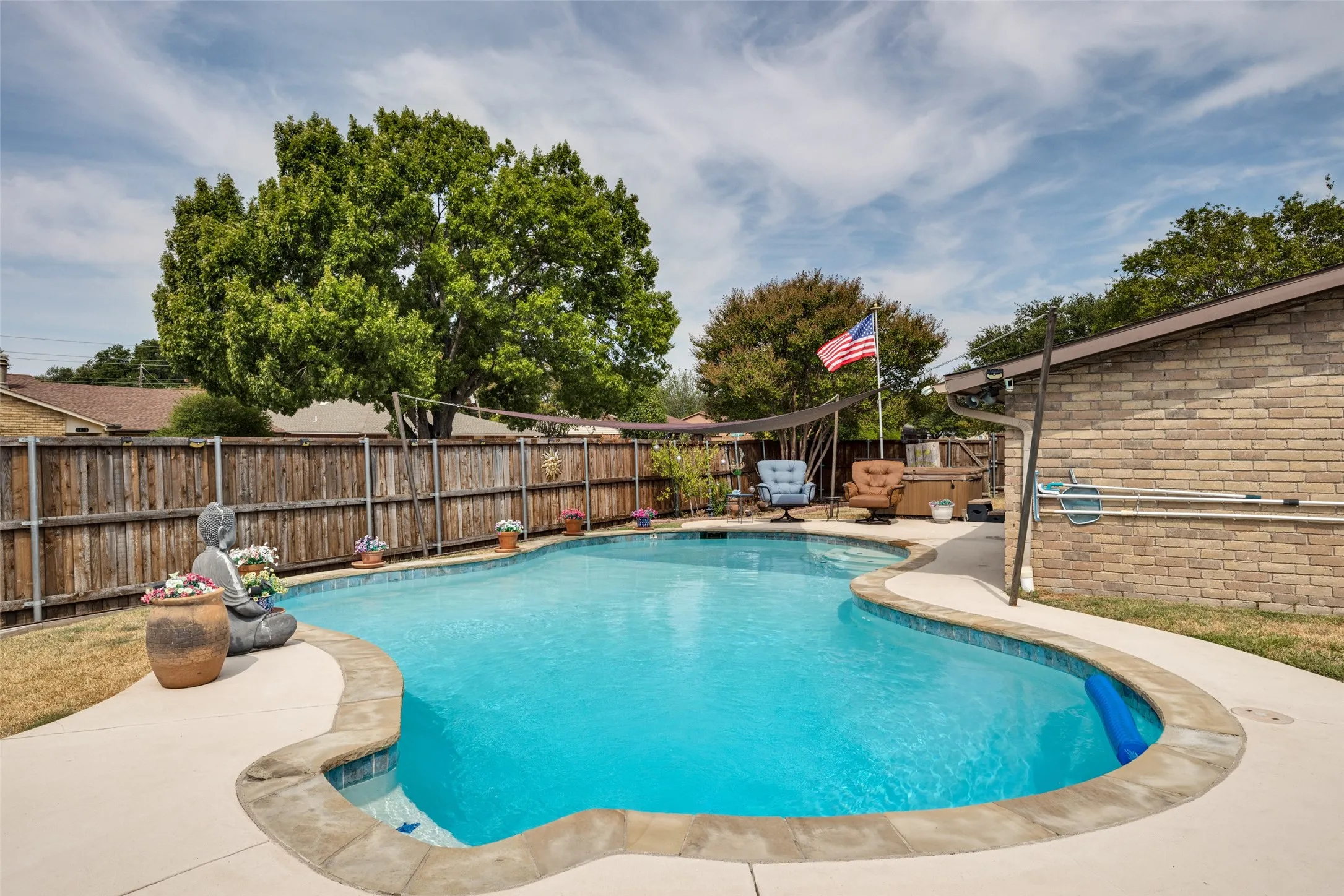 Freeform swimming pool with concrete decking, wood privacy fencing, and a brick-clad exterior