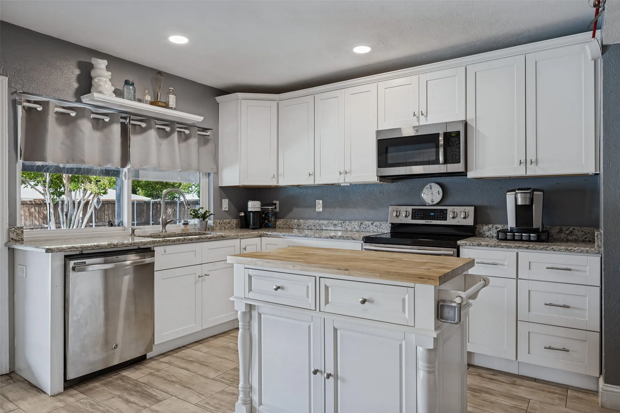 Kitchen featuring white shaker cabinetry, stainless steel appliances, granite countertops, wood-finish flooring, and a kitchen island with a butcher block top