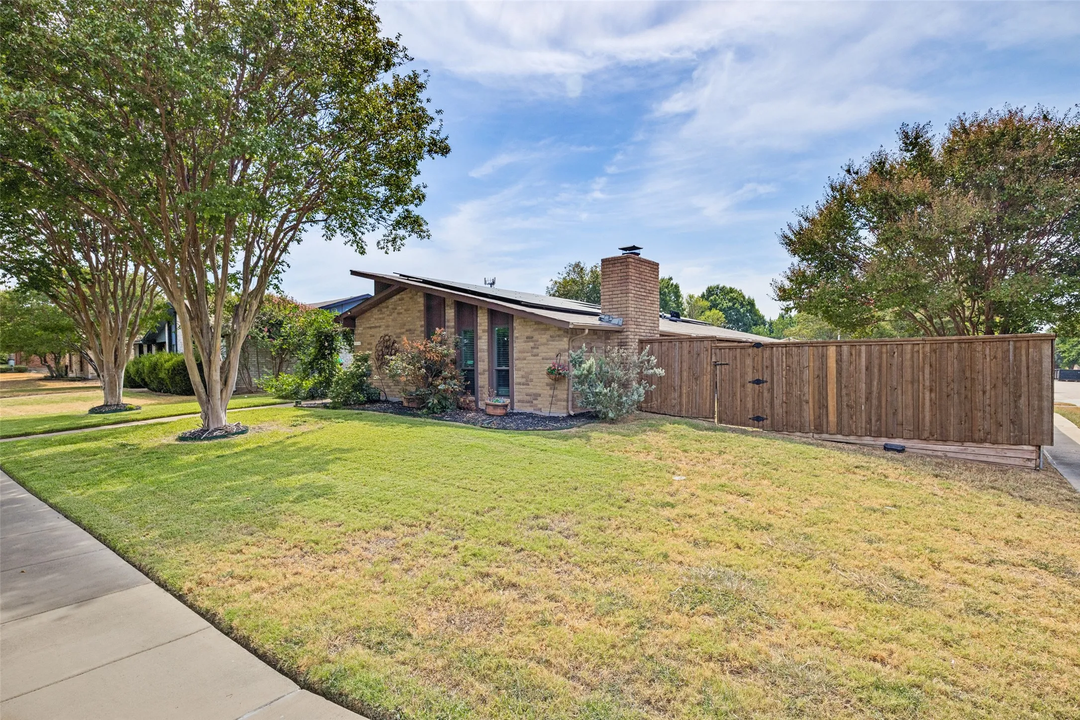 Brick exterior residence with a wood privacy fence, mature trees, and a concrete sidewalk