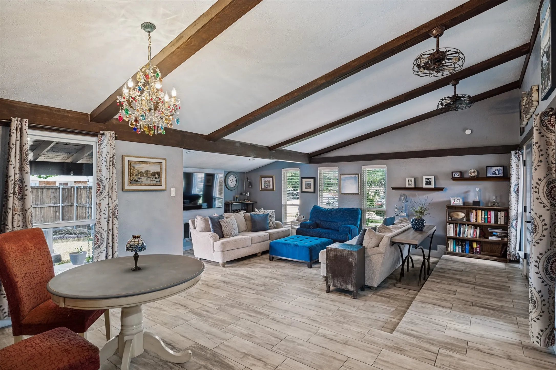 Vaulted ceiling with exposed wood beams, wood-finish flooring, multiple windows, built-in shelving, and a decorative chandelier