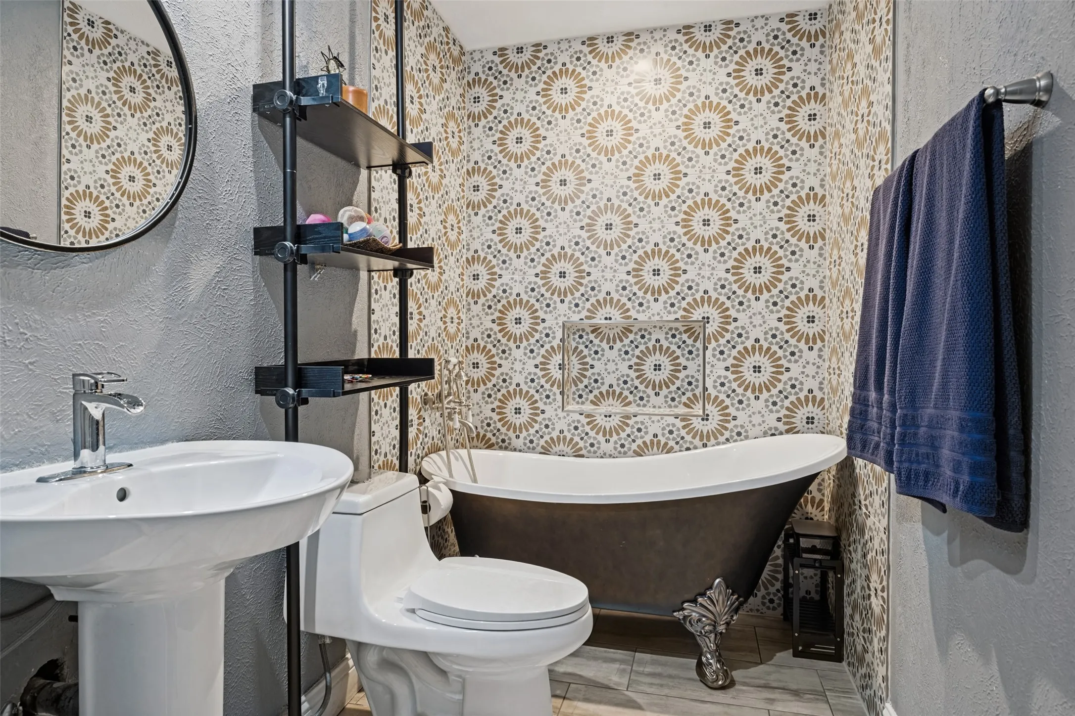 Pedestal sink with chrome faucet, floor-mounted toilet, freestanding clawfoot bathtub, patterned tile wall, and built-in shelving unit