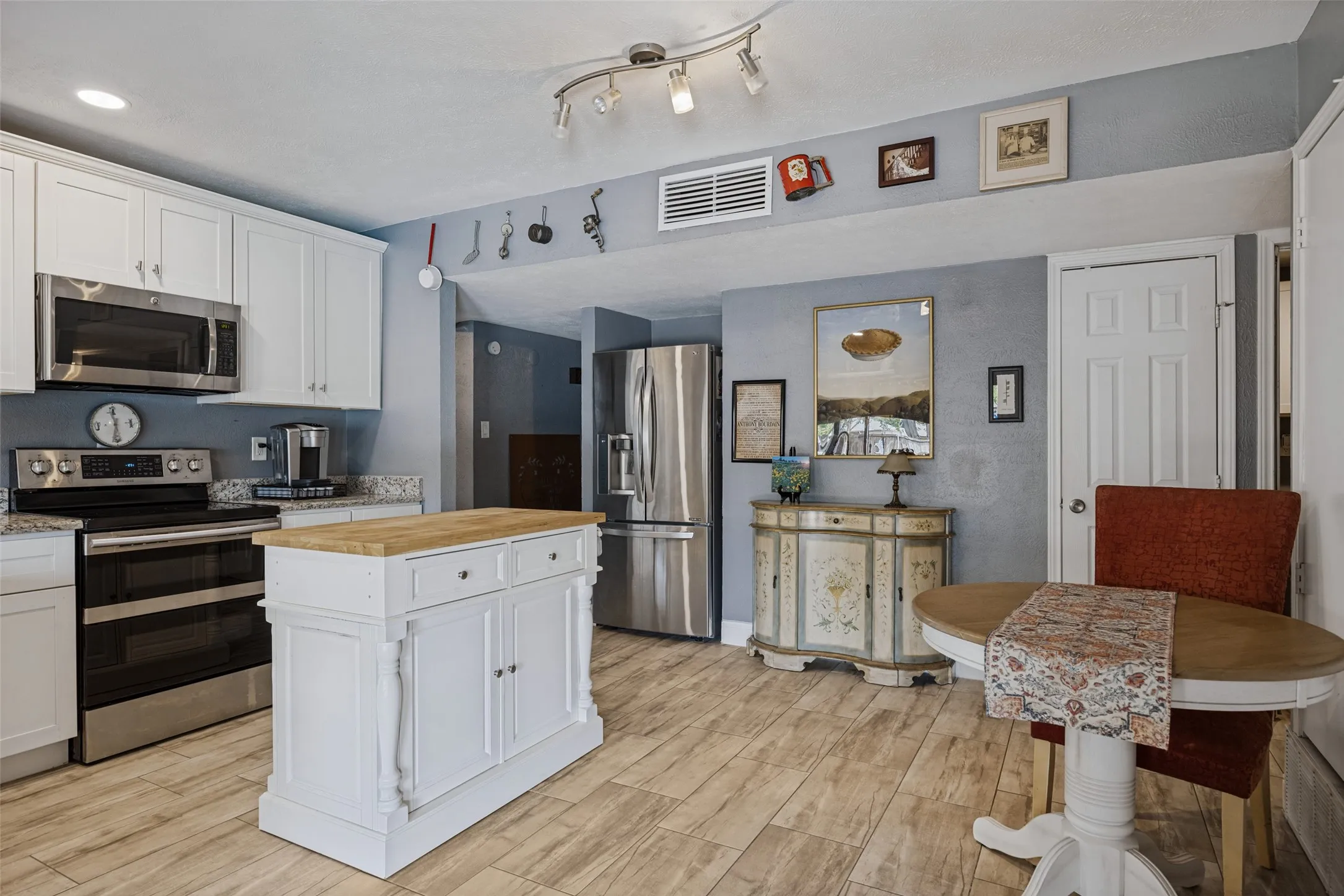 Kitchen featuring stainless steel appliances, white cabinetry, a butcher block island, and wood-finish flooring