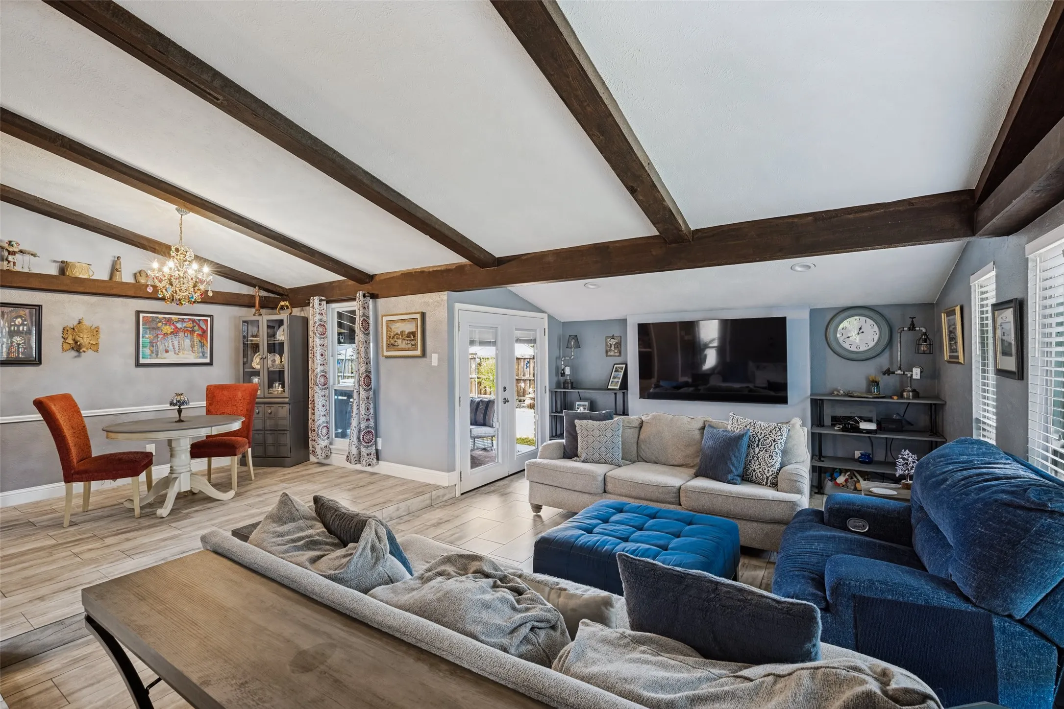 Vaulted ceiling with exposed wood beams, French doors, chandelier, wood-finish flooring, and built-in shelving