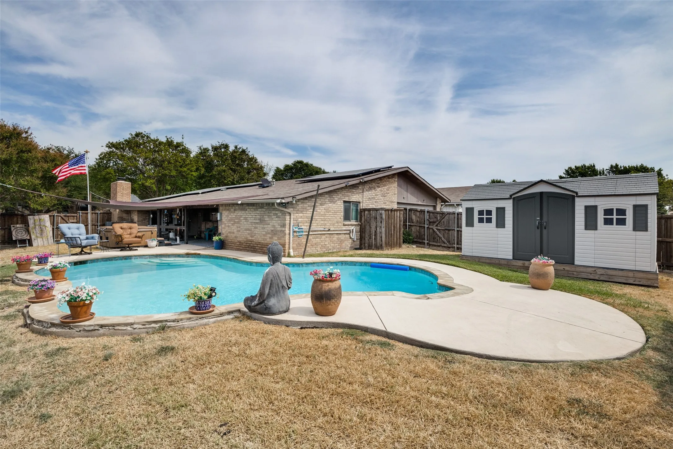 Outdoor pool with a concrete surround, accompanied by a detached storage shed featuring double doors and window details