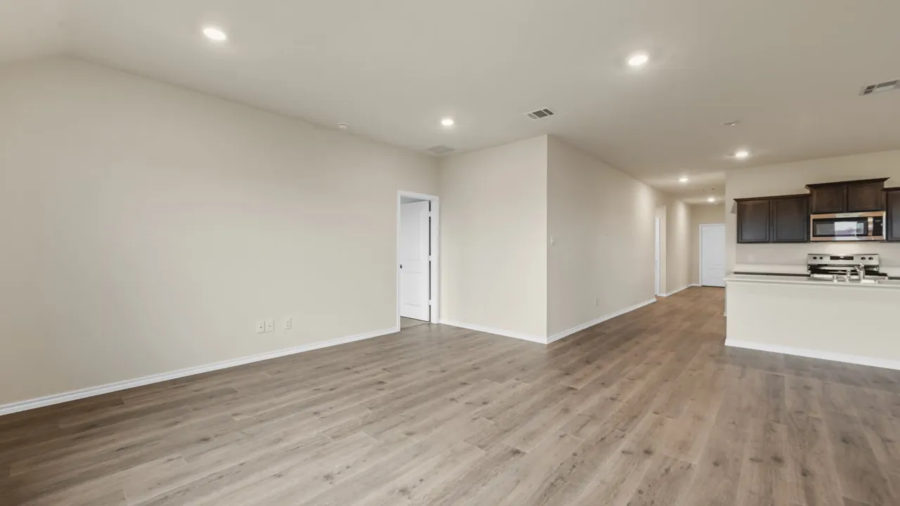 Open-concept living area featuring wood-finish flooring, recessed lighting, and a kitchen with dark wood cabinetry, stainless steel appliances, and a light-toned countertop