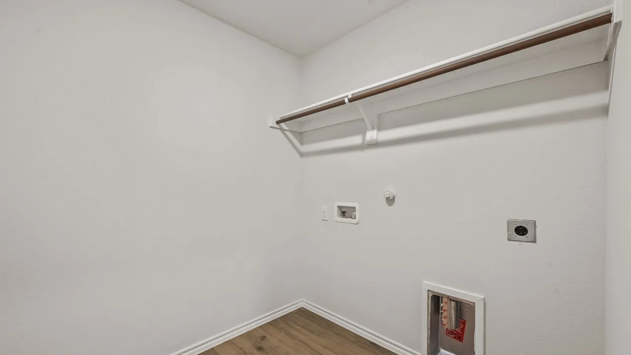 Wood-finish flooring with white baseboards, wall-mounted clothes rod, and utility hookups