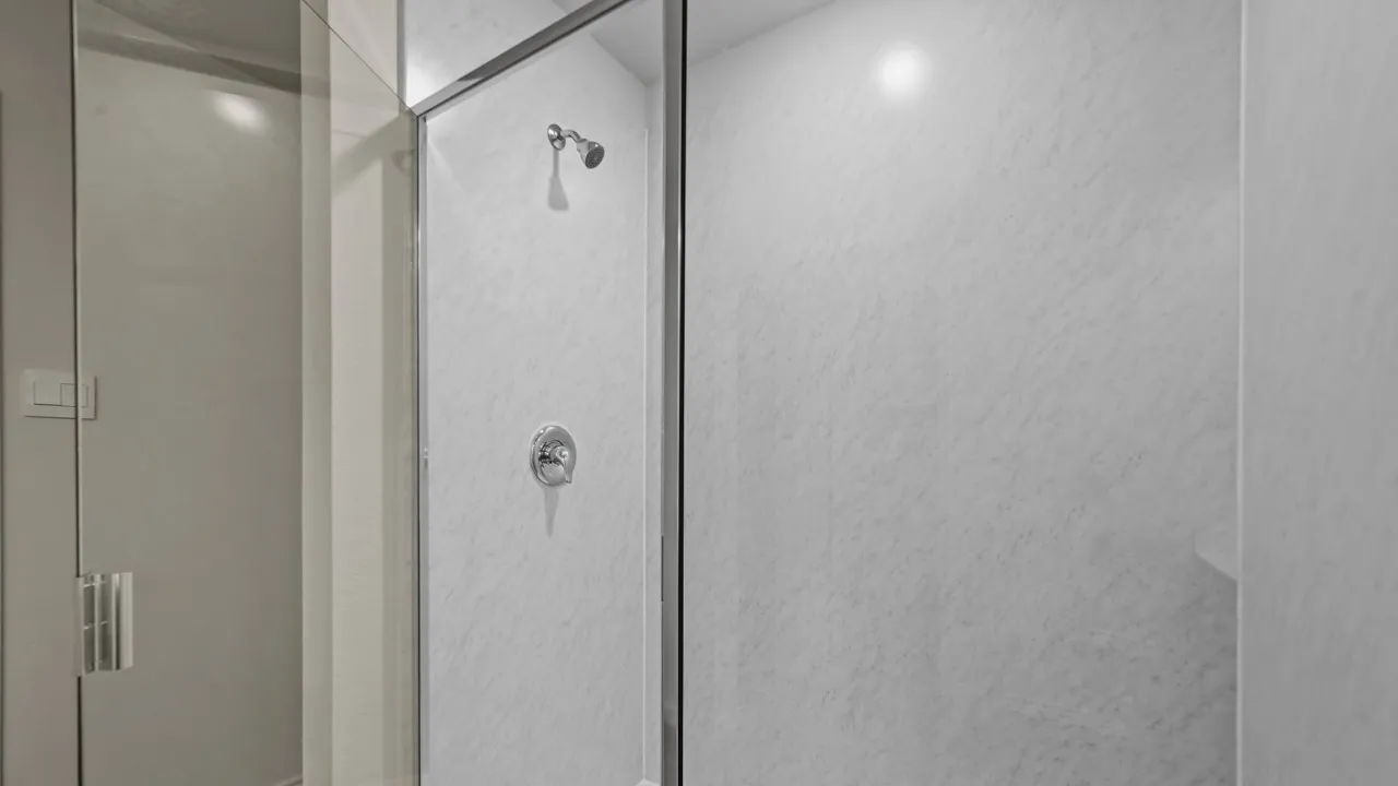 Glass-enclosed shower with a chrome shower head and control