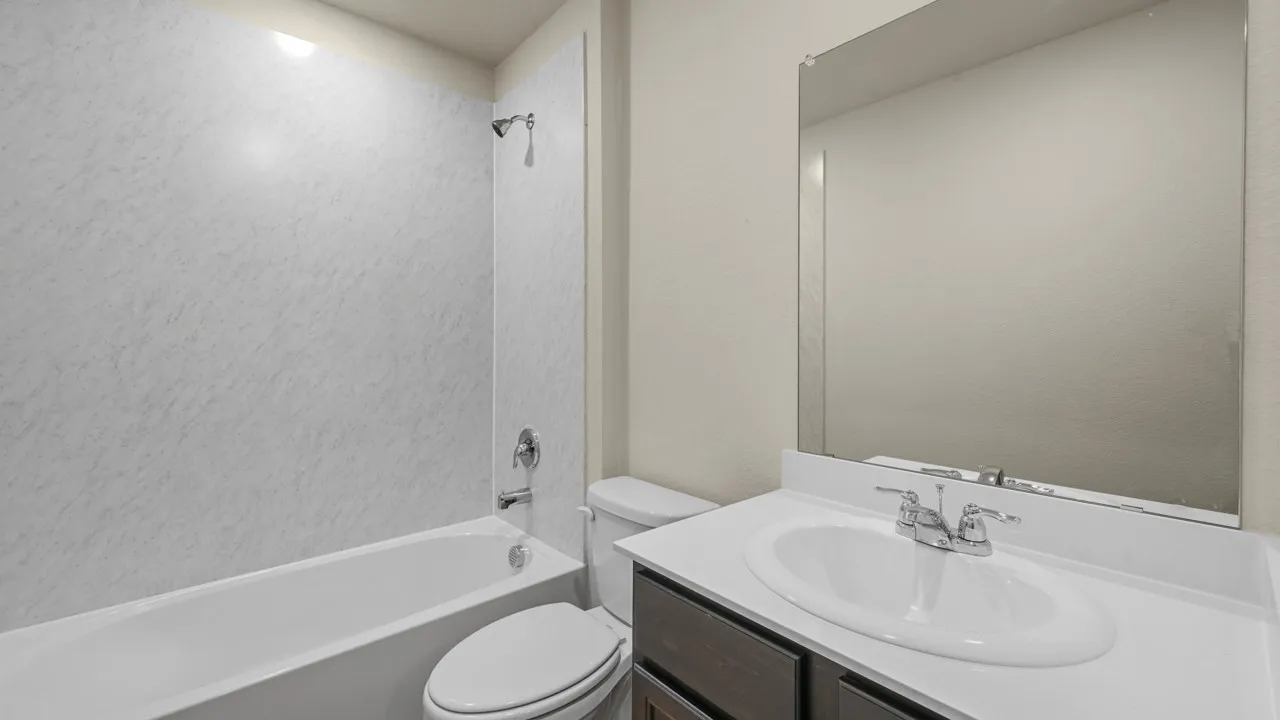 White bathtub with a built-in shower, vanity with a white countertop, and a large wall-mounted mirror