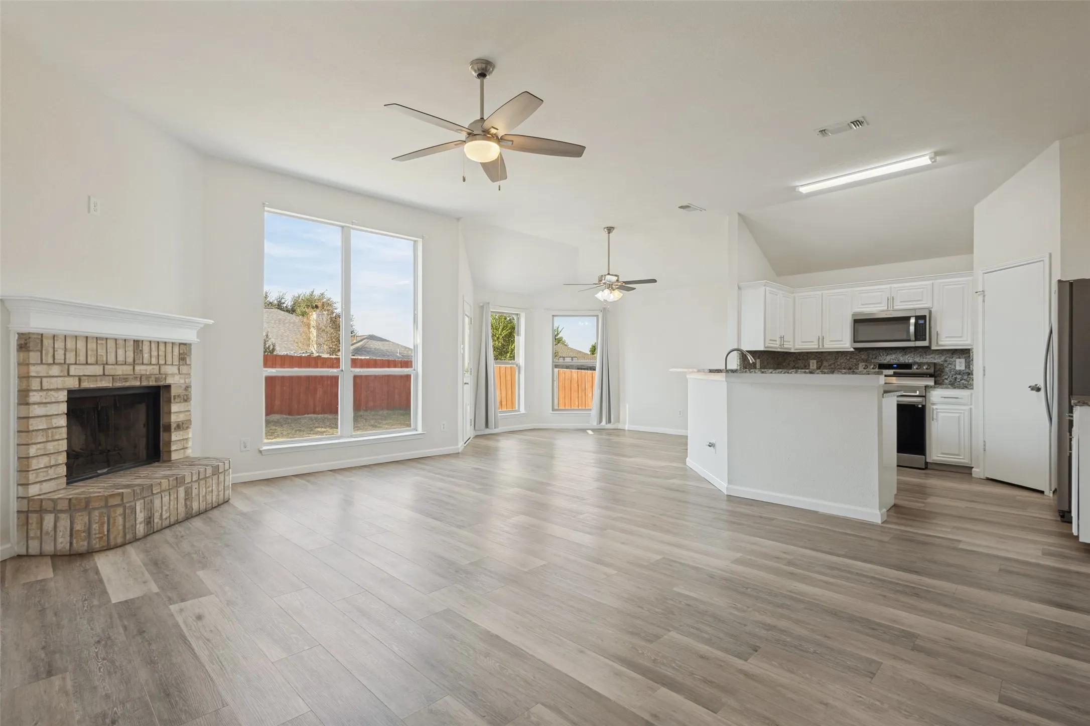 Spacious living area featuring light wood-finish flooring, a brick fireplace, and vaulted ceilings