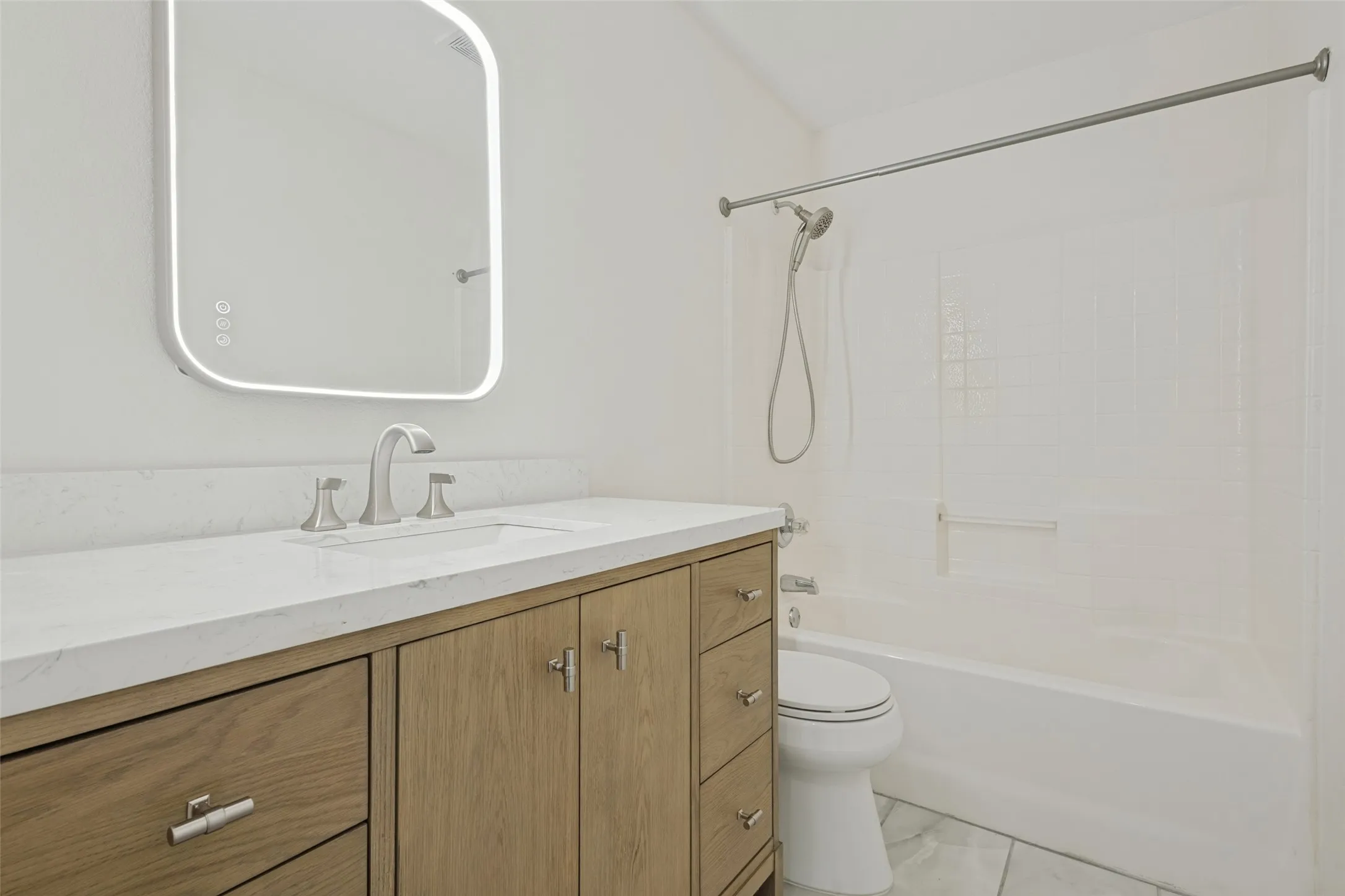 Bathroom featuring a white bathtub with a shower head, wood-finish vanity with a white countertop, and a lighted mirror