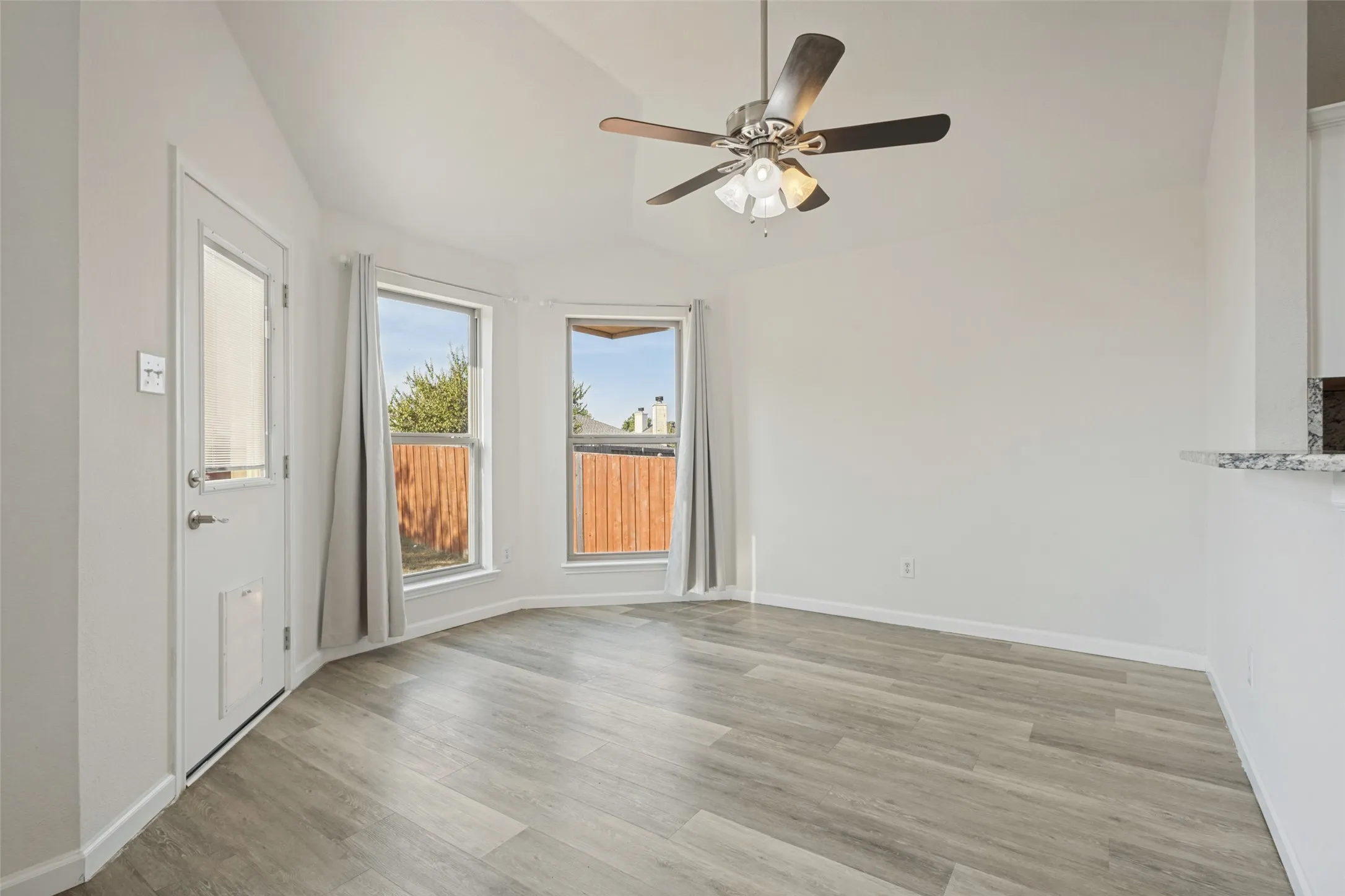 Vaulted ceiling with a ceiling fan, wood-finish flooring, two large windows, and a door with a glass insert