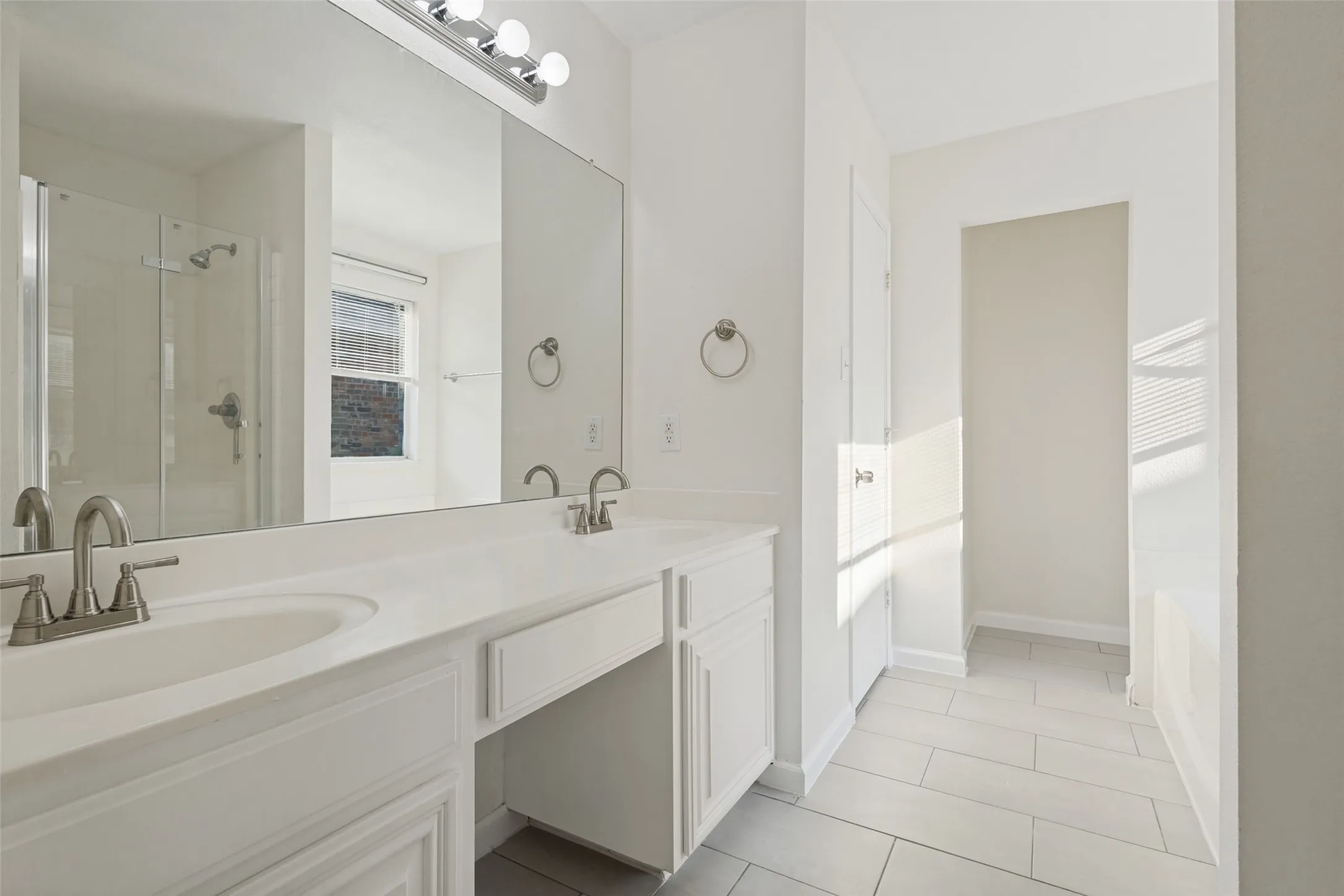 Dual sink vanity with white cabinetry, brushed nickel fixtures, a large wall-mounted mirror, and tile flooring