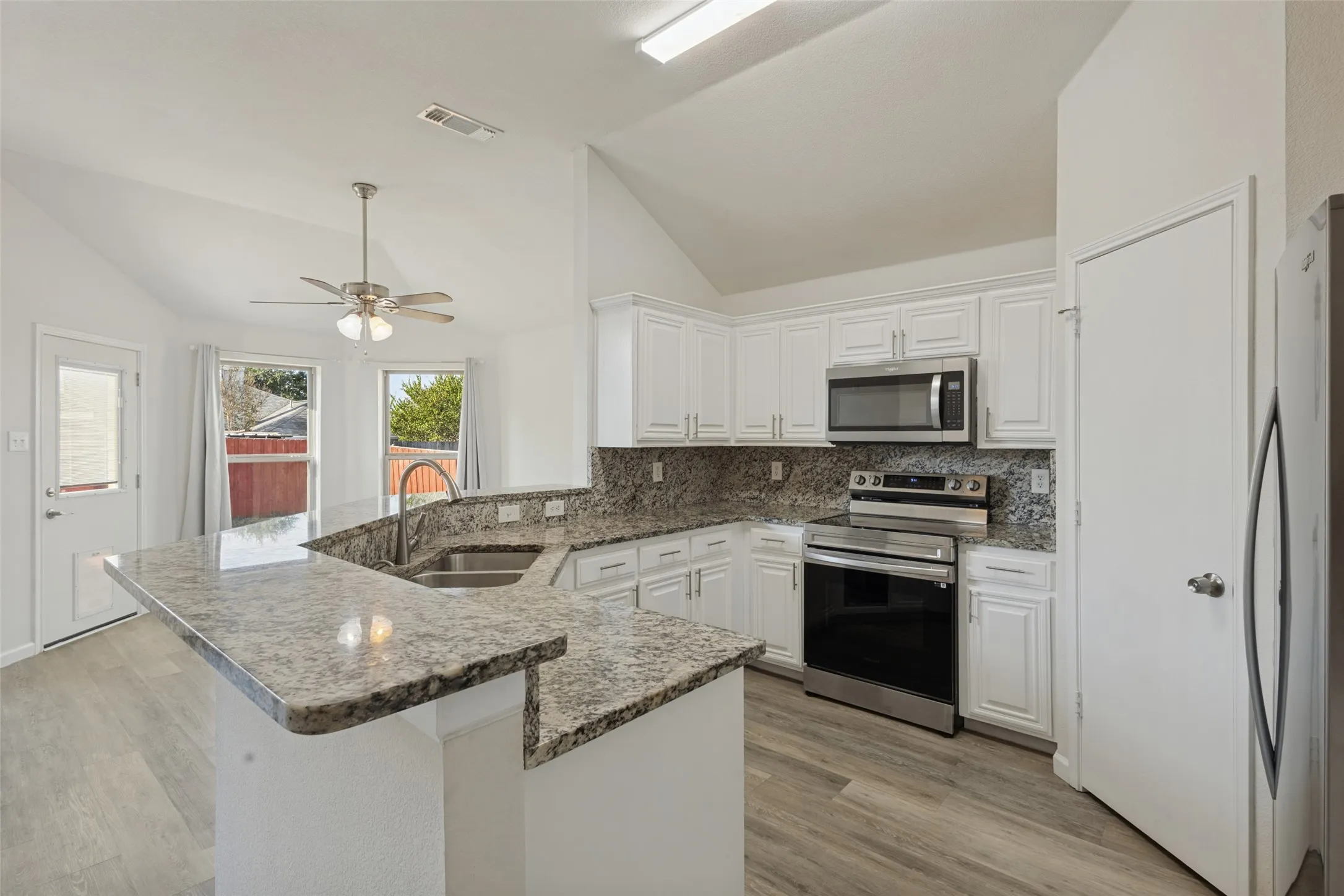 Vaulted ceiling, wood-finish flooring, white cabinetry, stainless steel appliances, and granite countertops
