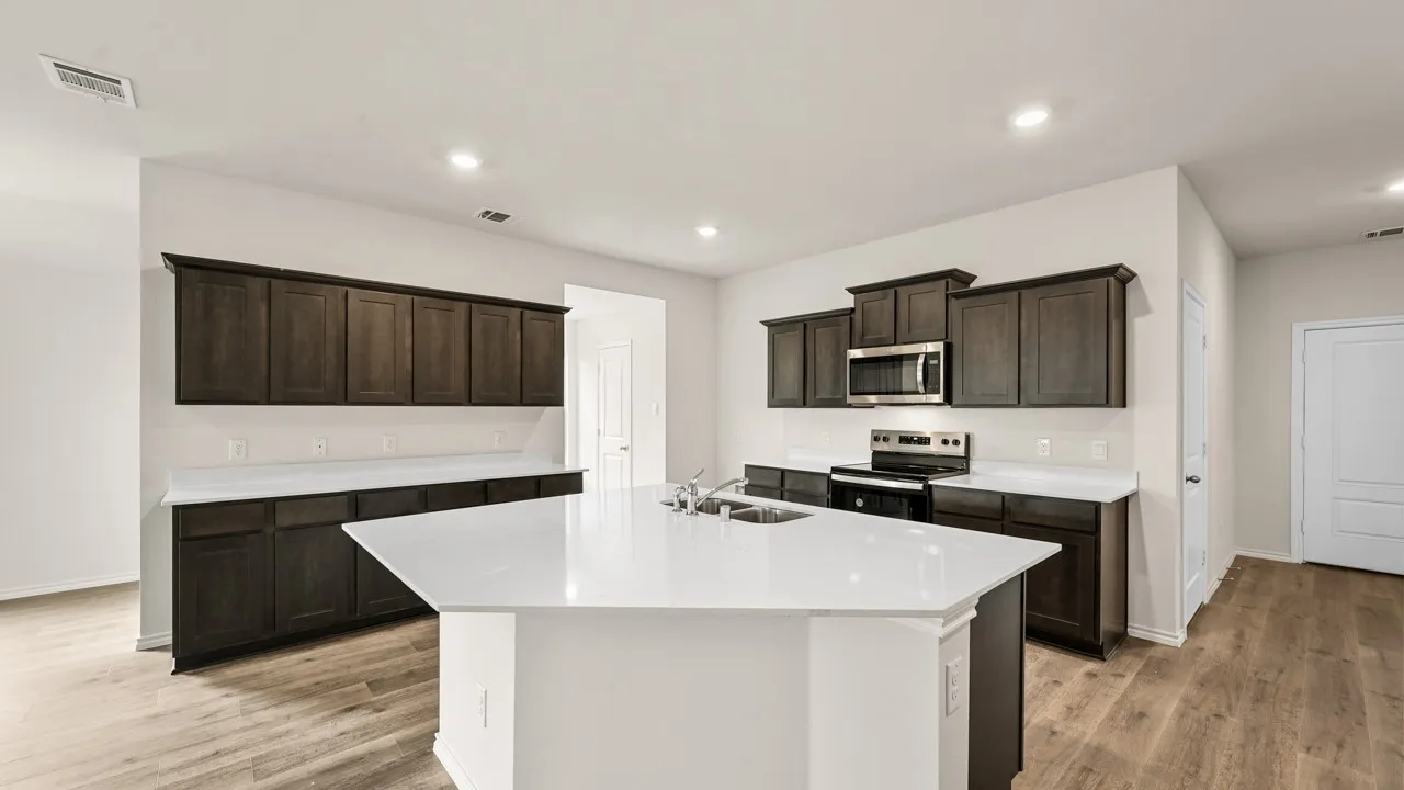 Kitchen featuring a large island with sink, dark wood-finish cabinetry, white countertops, stainless steel microwave, and wood-finish flooring