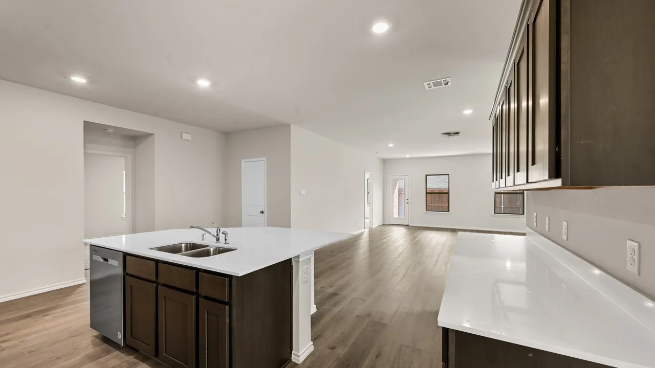 Open-concept living space with wood-finish flooring, recessed lighting, and a kitchen island featuring a dual basin sink