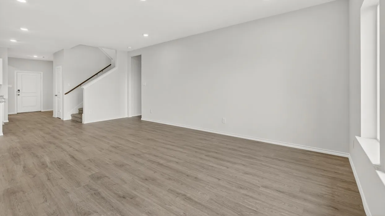 Open-concept living space with wood-finish flooring, recessed lighting, white walls, and a staircase with a dark wood handrail