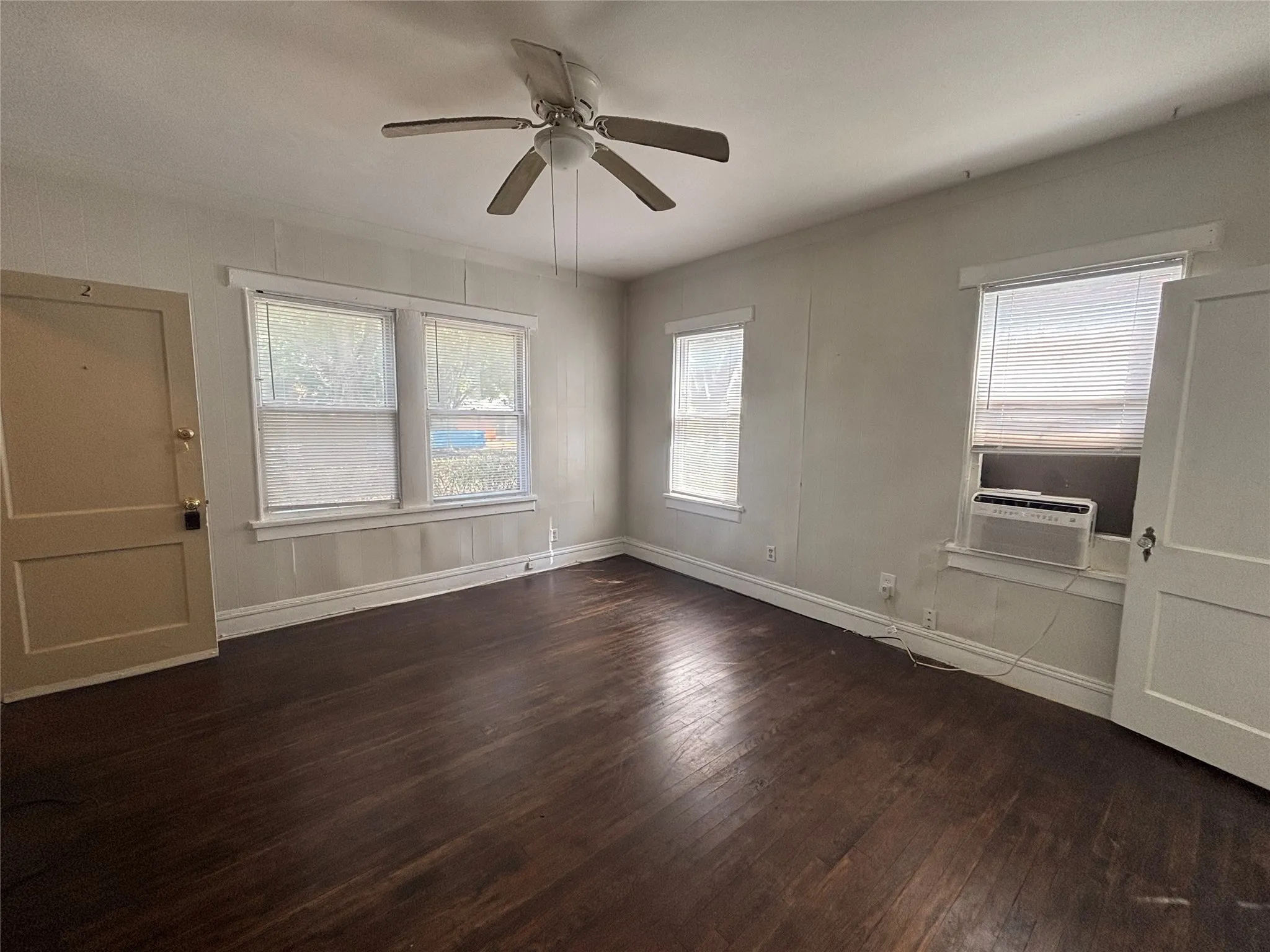 Hardwood flooring, multiple windows, ceiling fan, and white trim throughout
