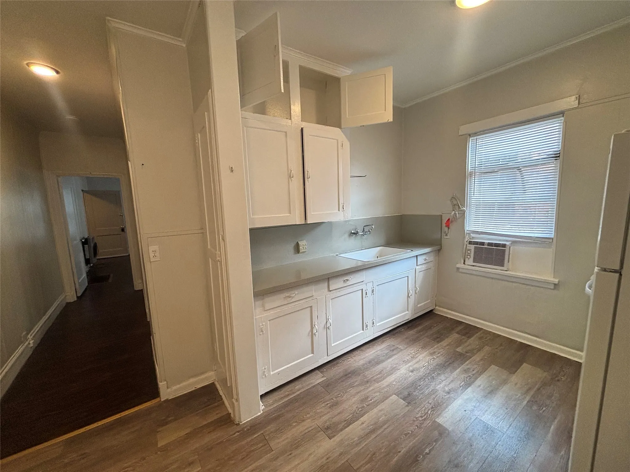 Kitchen featuring wood-finish flooring, built-in white cabinetry, a single basin sink, and an integrated window unit