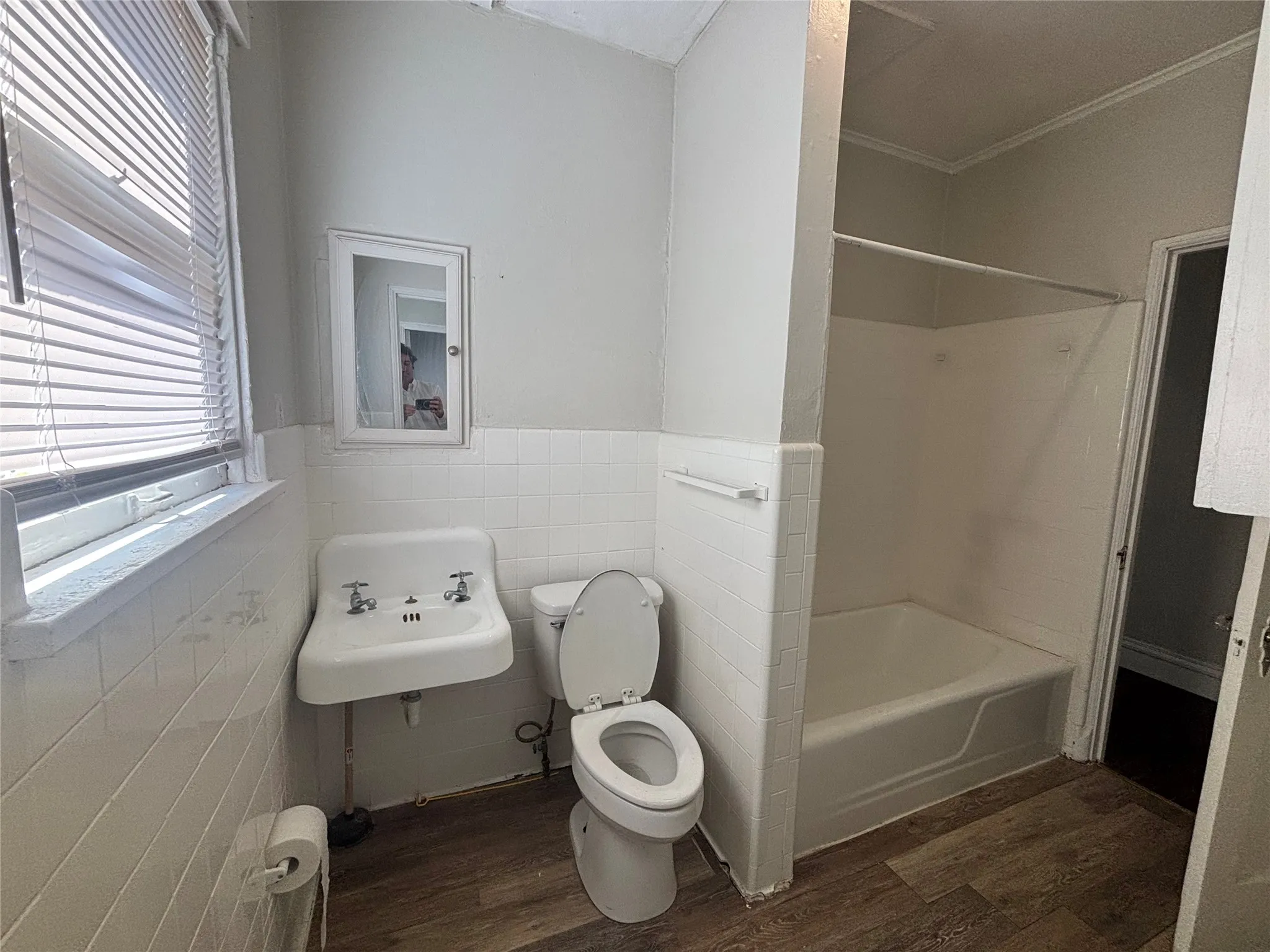 Bathroom featuring a wall-mounted sink, a toilet, a bathtub, and wood-finish flooring
