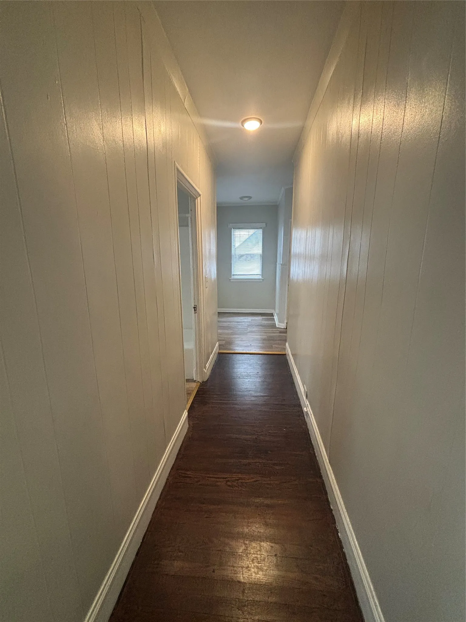 Wood-finish flooring extending through the hallway, vertical paneling on walls, and ceiling-mounted lighting