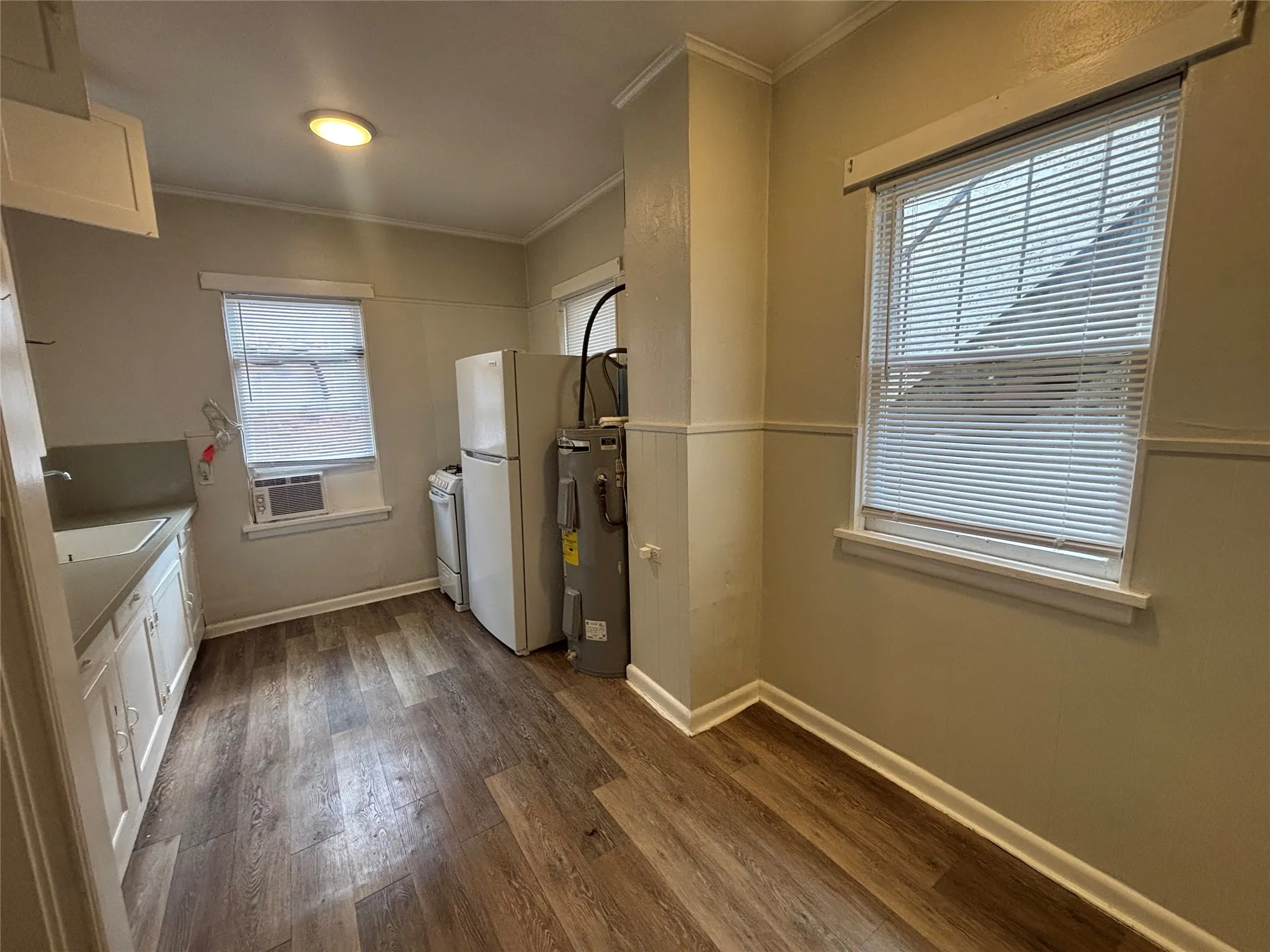 Wood-finish flooring, white cabinetry, a built-in sink, and two windows with blinds