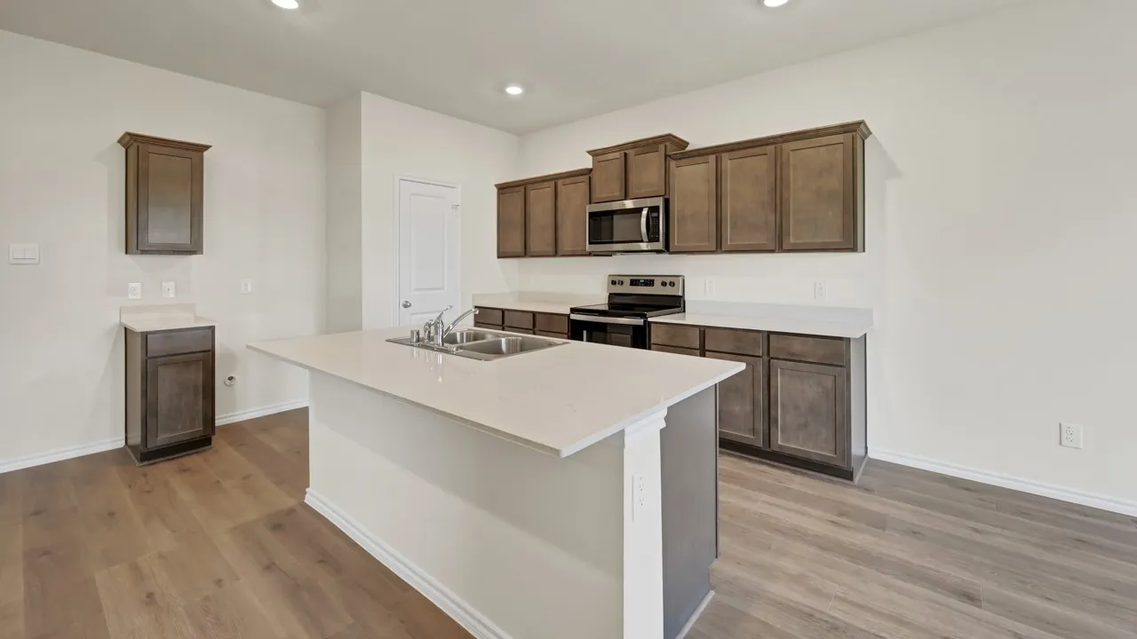 Kitchen featuring wood-finish flooring, dark wood cabinetry, light countertops, and a stainless steel microwave