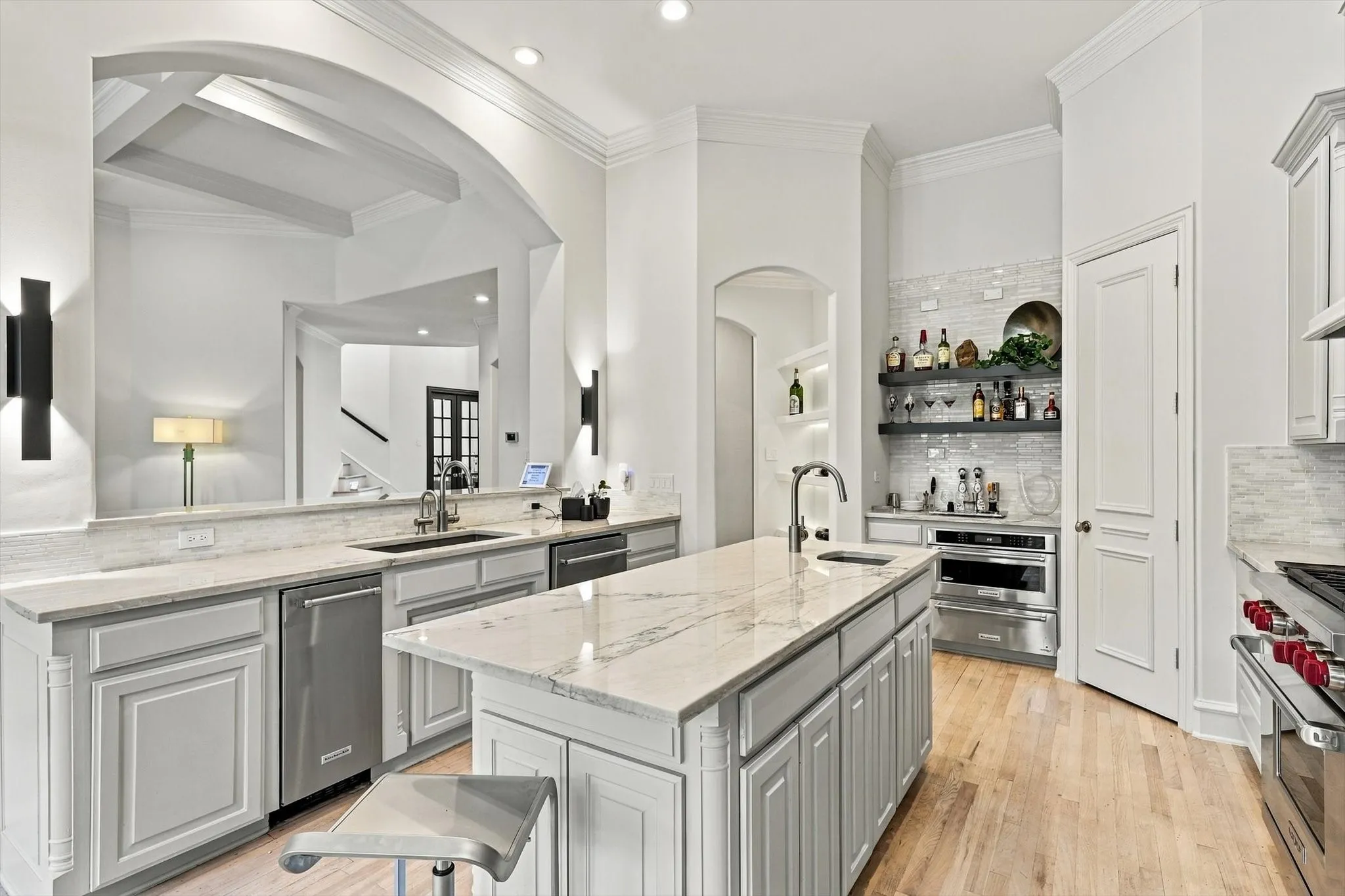 Kitchen featuring light-finish cabinetry, light-toned countertops, a central island with an integrated sink, stainless steel appliances, and wood-finish flooring