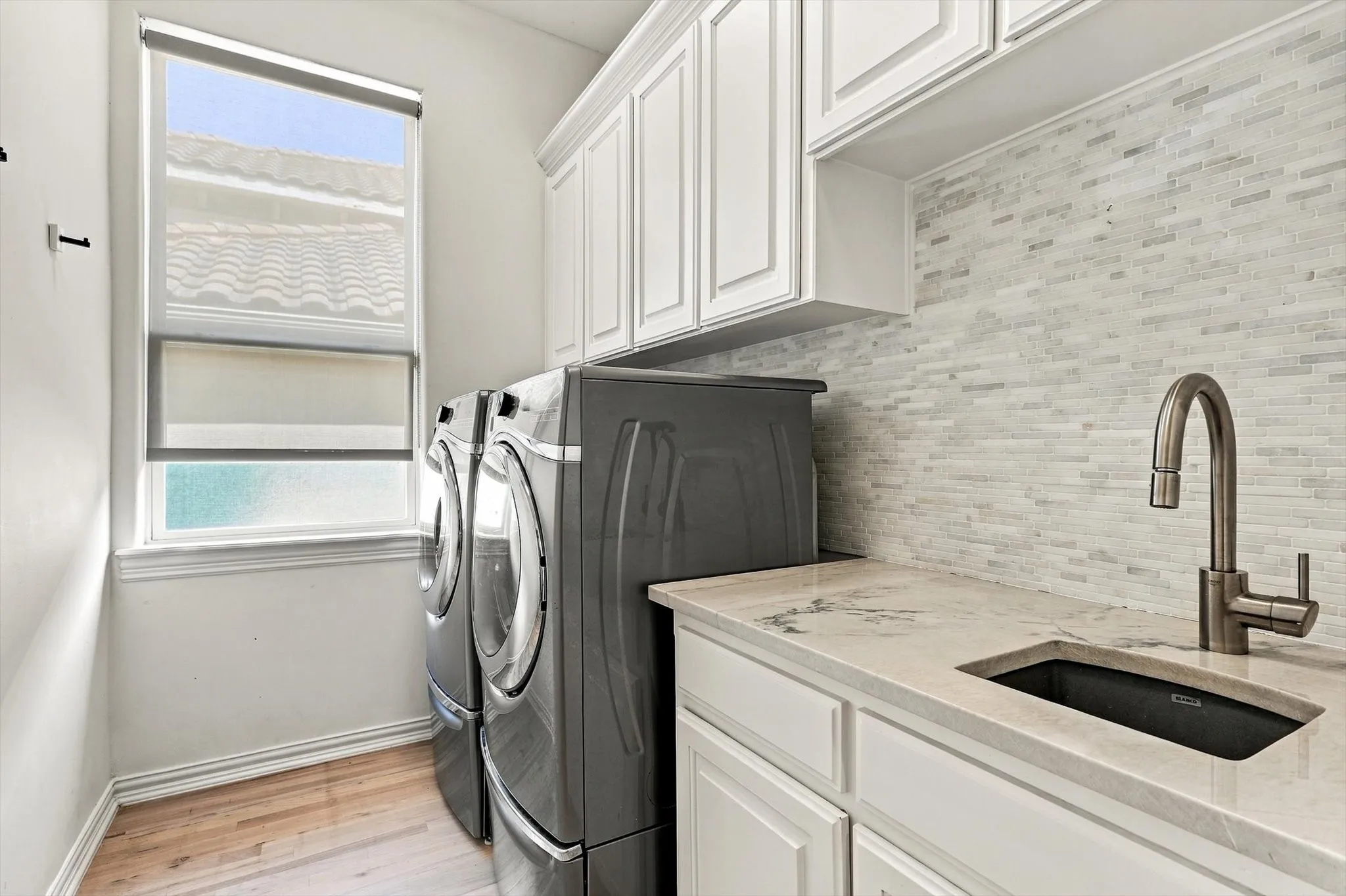 Laundry room featuring wood-finish flooring, white cabinetry, a light-toned countertop, a rectangular undermount sink, and a stacked tile backsplash