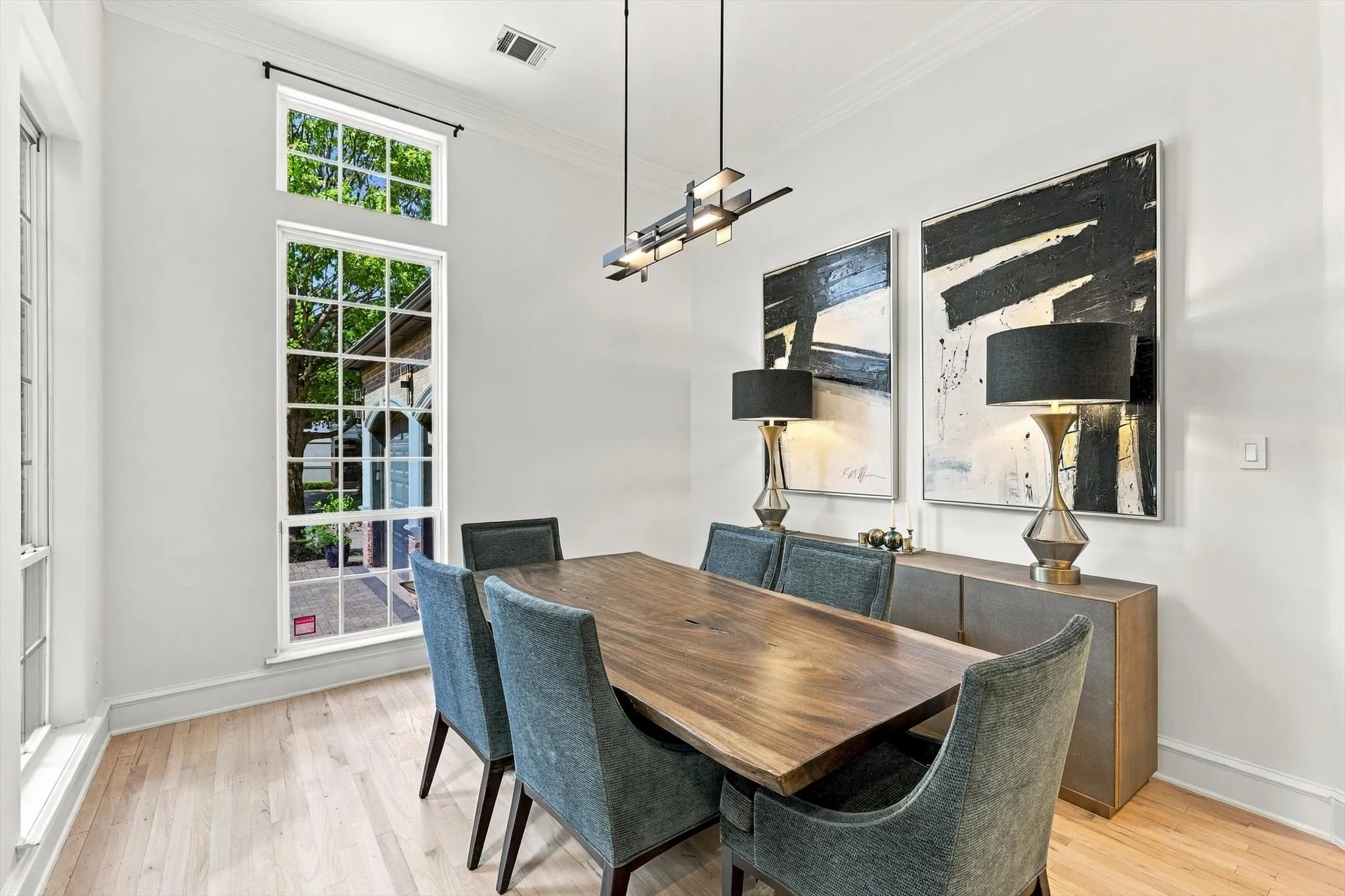 Light wood-finish flooring with white baseboards, crown molding, and a modern linear chandelier