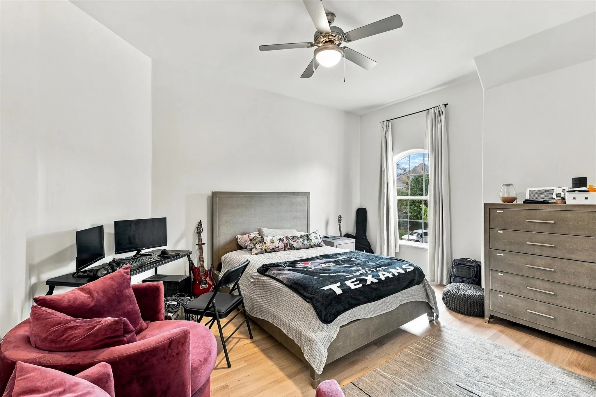 Wood-finish flooring, ceiling fan with integrated lighting, arched window, and neutral wall tones