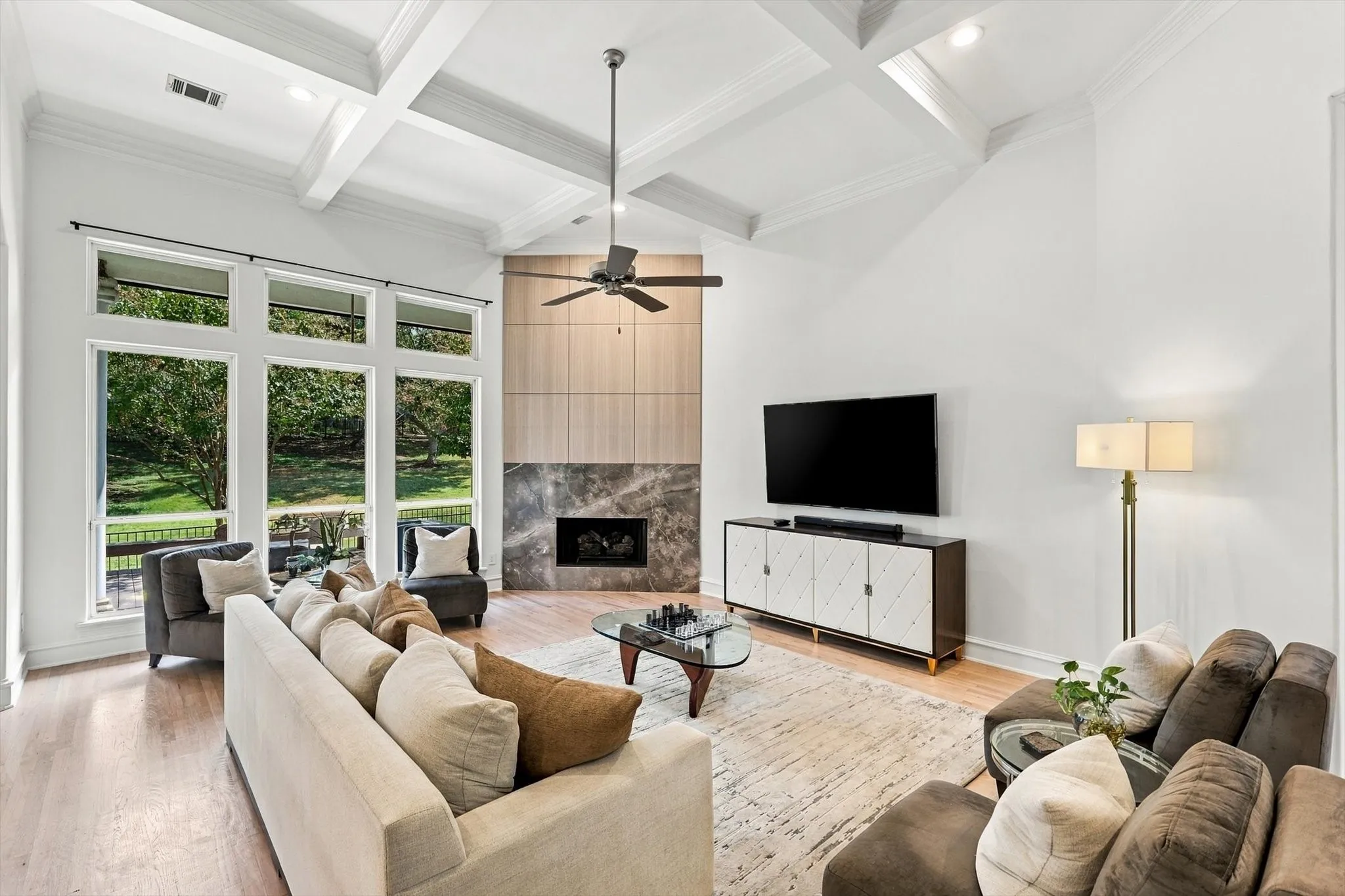 Vaulted coffered ceiling with a ceiling fan, wide plank wood-finish flooring, and a fireplace featuring a stone surround and wood paneling