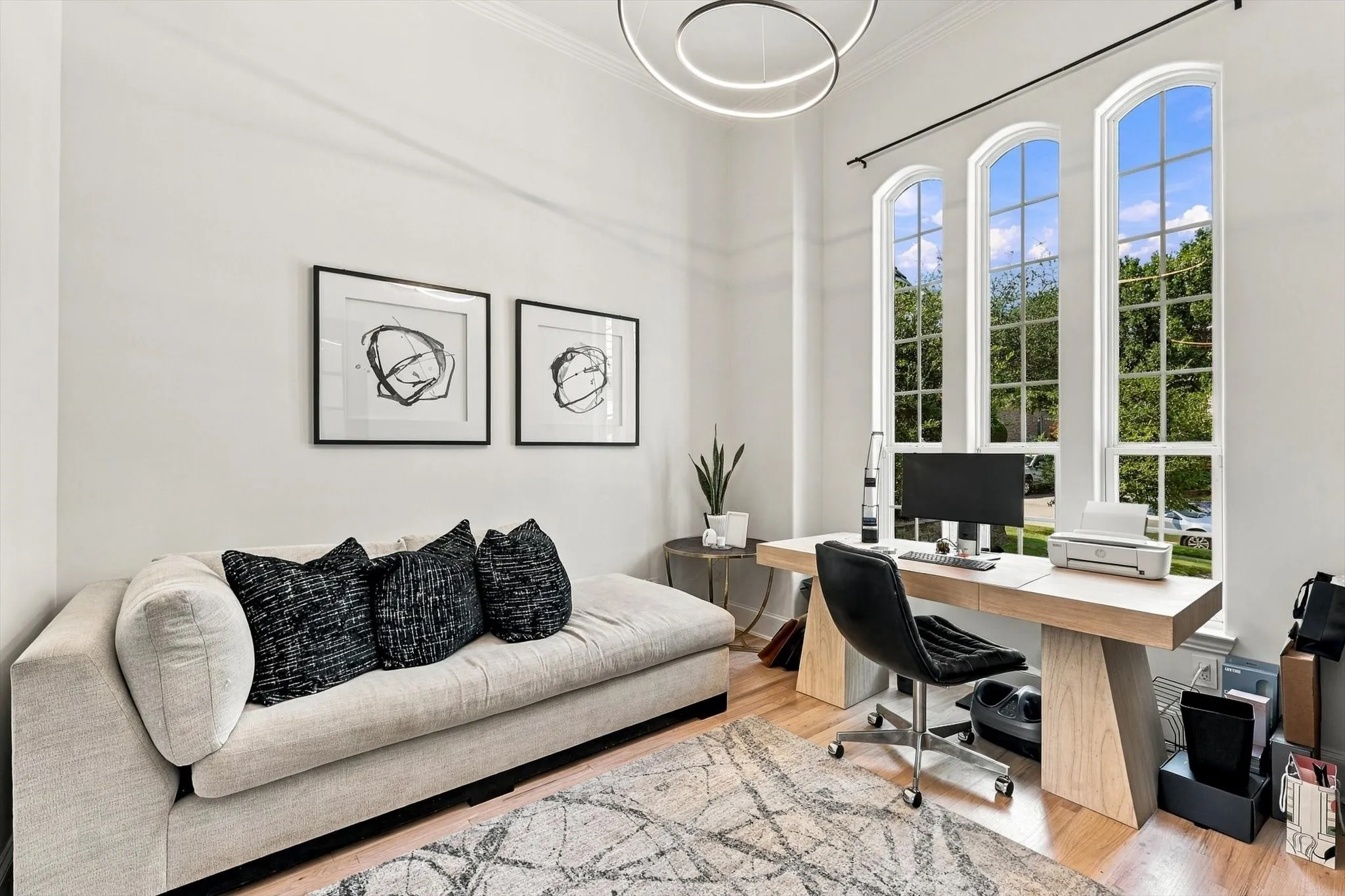 High ceilings with crown molding, three arched windows, light wood-finish flooring, and a contemporary ceiling light fixture