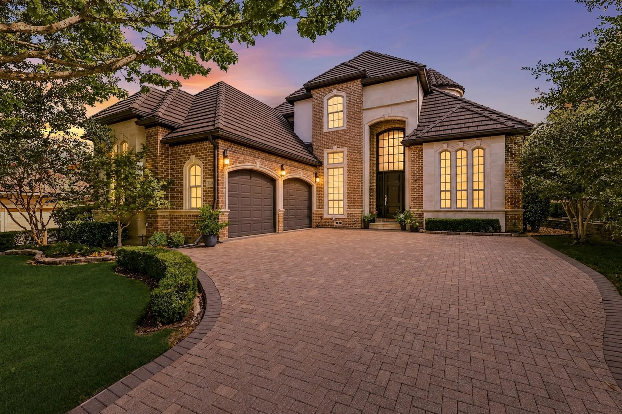 Brick and stucco facade with arched windows, a paver driveway, and a two-car garage