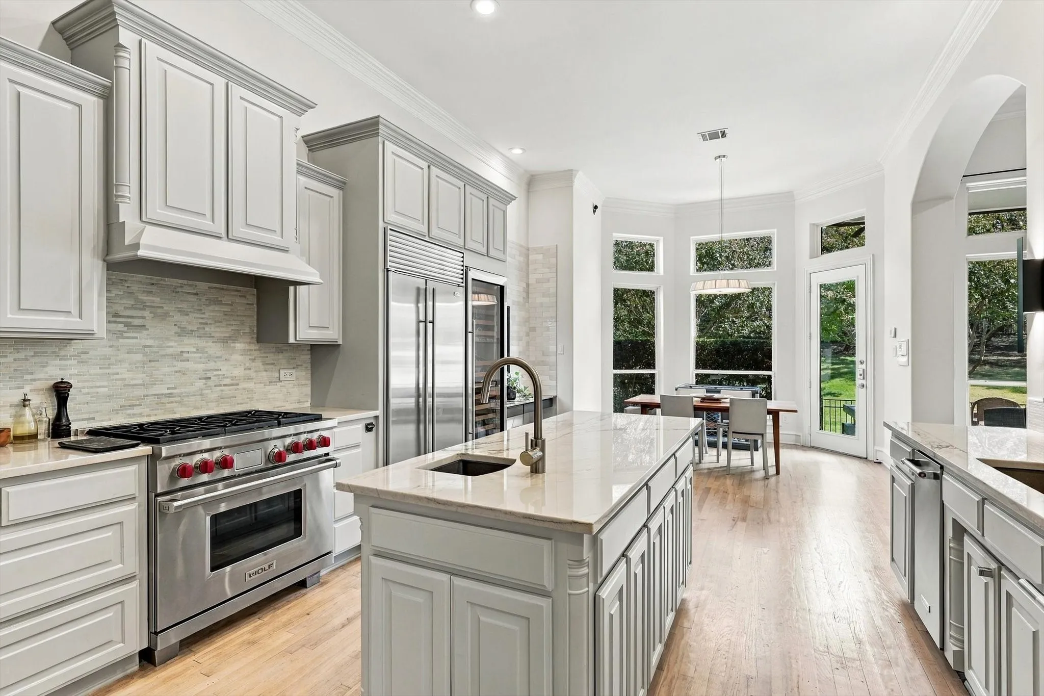 Gourmet kitchen with stainless steel appliances, central island with sink, light-toned wood-finish flooring, and a dining area with expansive windows