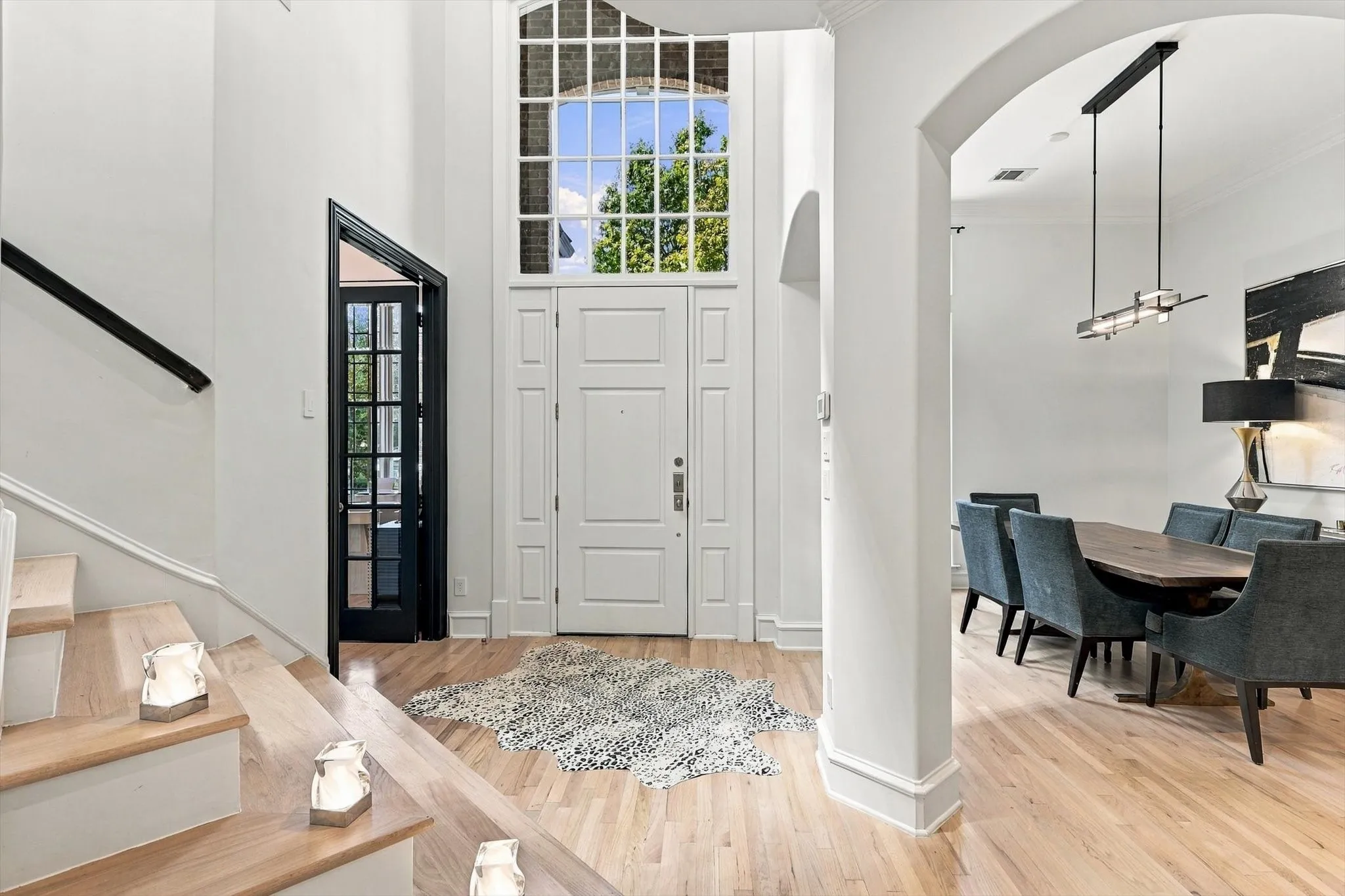 Light wood-finish flooring, white paneled entry door with transom window, and black French doors with clear glass panels