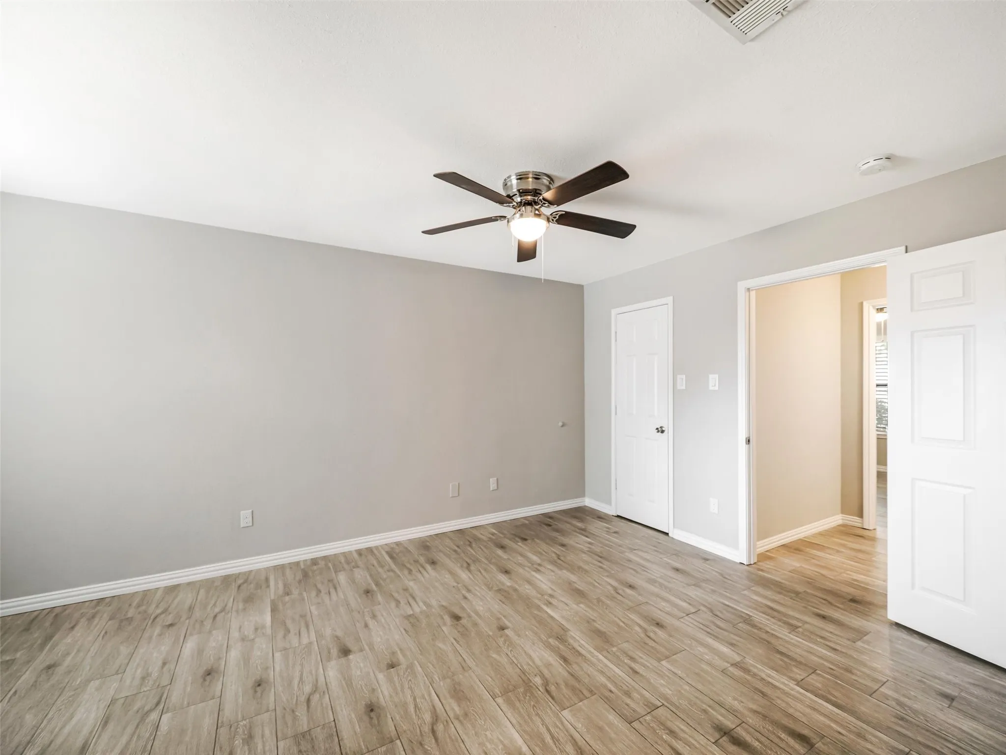 Generous room with wood-finish flooring, light gray walls, and a ceiling fan with integrated lighting