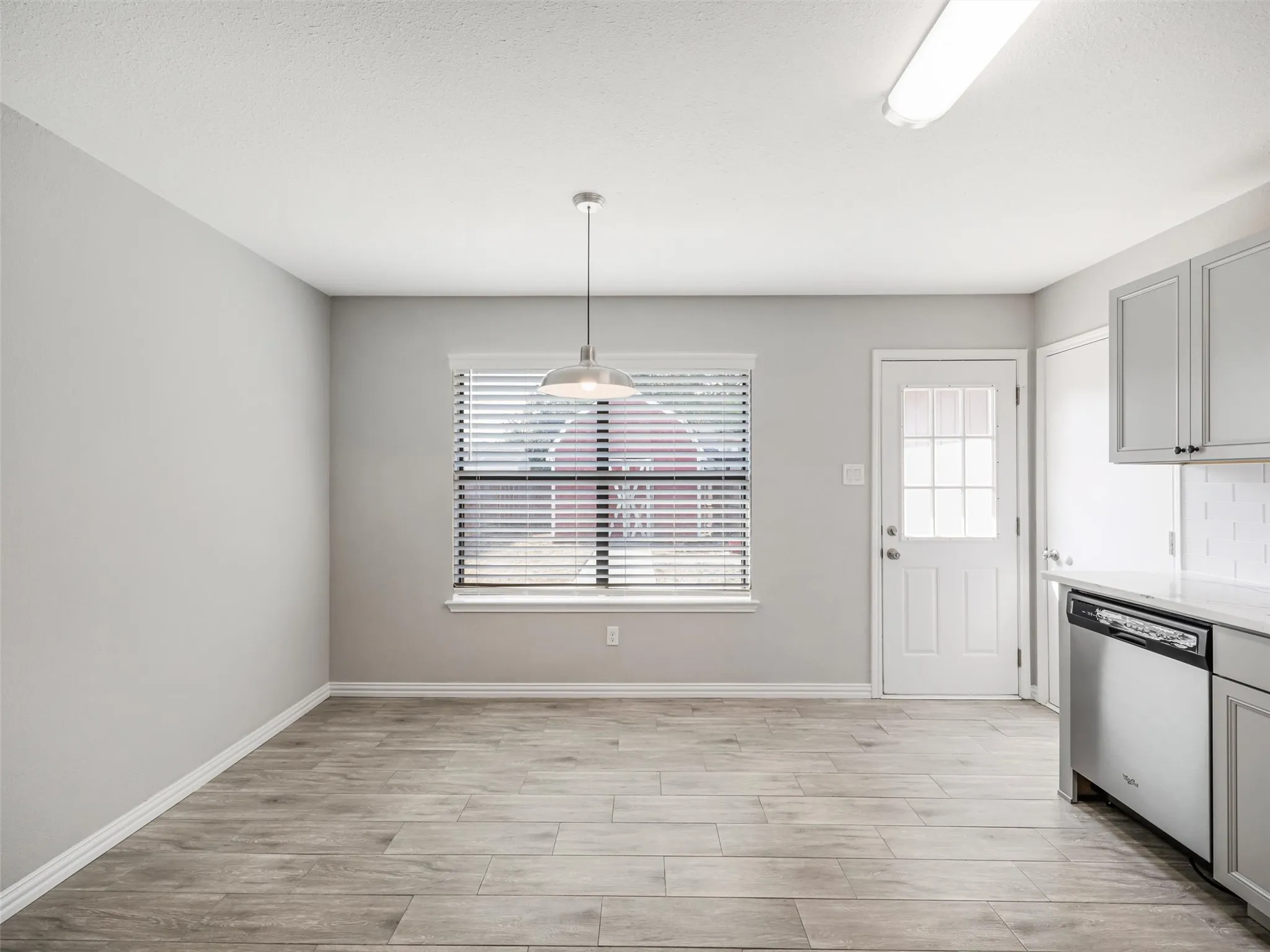Wood-finish flooring, a window with blinds, a pendant light fixture, a paneled door with glass inserts, and gray cabinetry