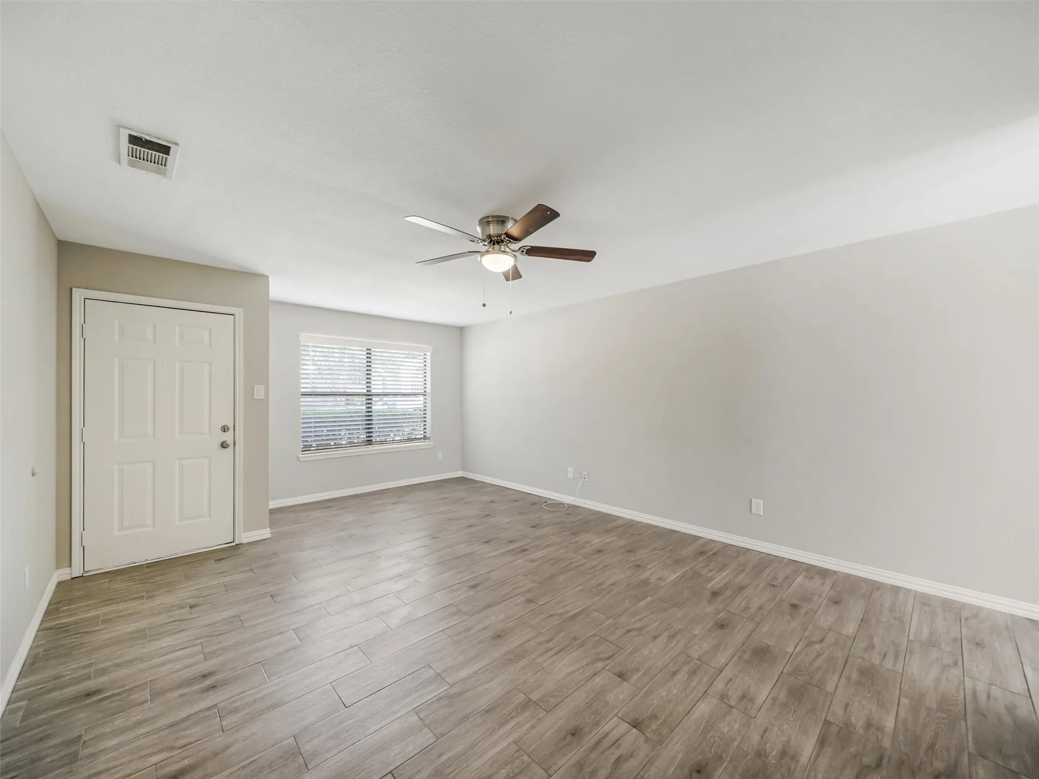 Neutral wall tones, wood-finish flooring, ceiling fan with integrated lighting, and window with blinds