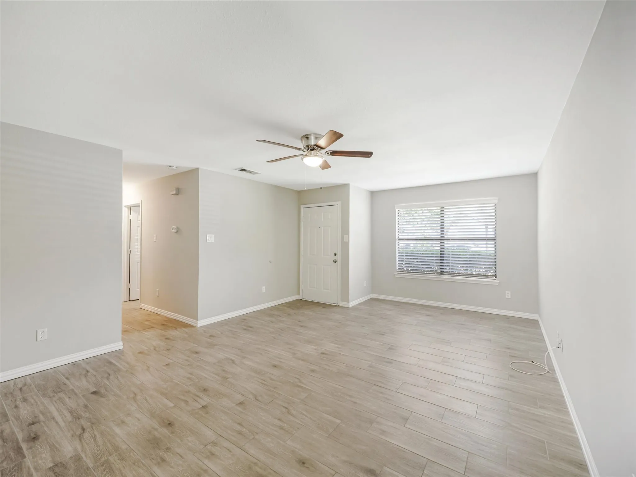 Spacious room featuring wood-finish flooring, a ceiling fan, and a large window with blinds