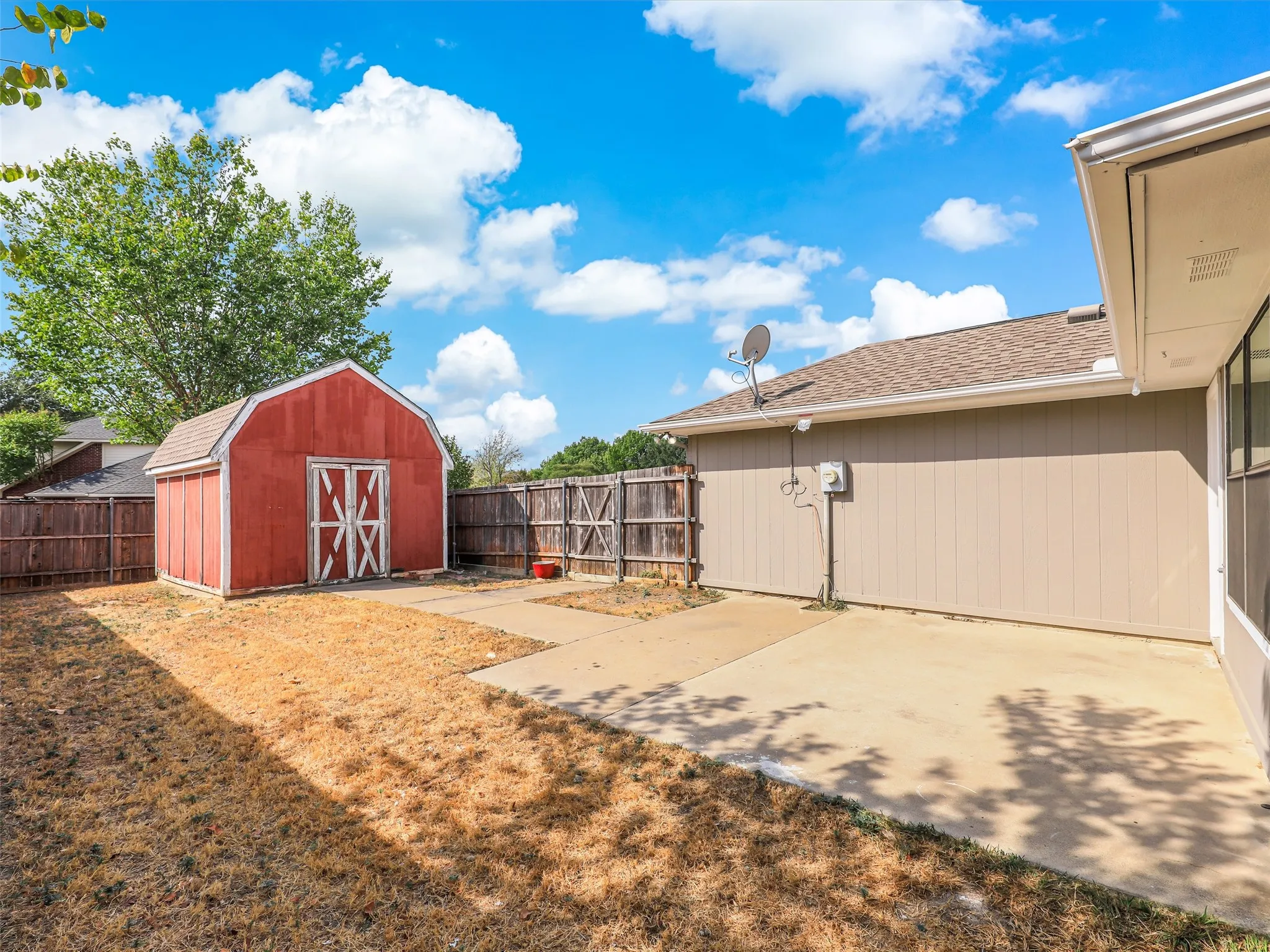 Concrete patio with attached dwelling, wood fence, and a detached red shed