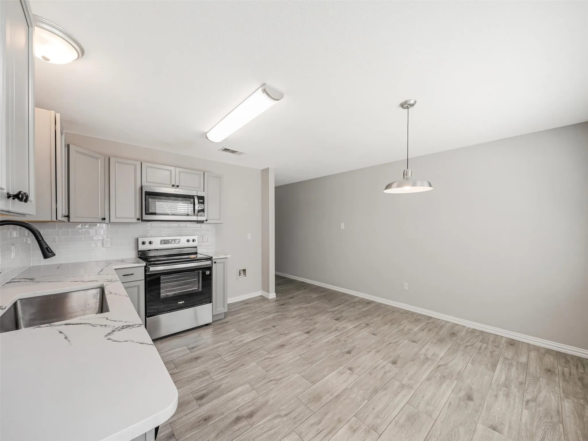 Kitchen featuring stainless steel appliances, light-toned cabinetry, subway tile backsplash, and wood-finish flooring
