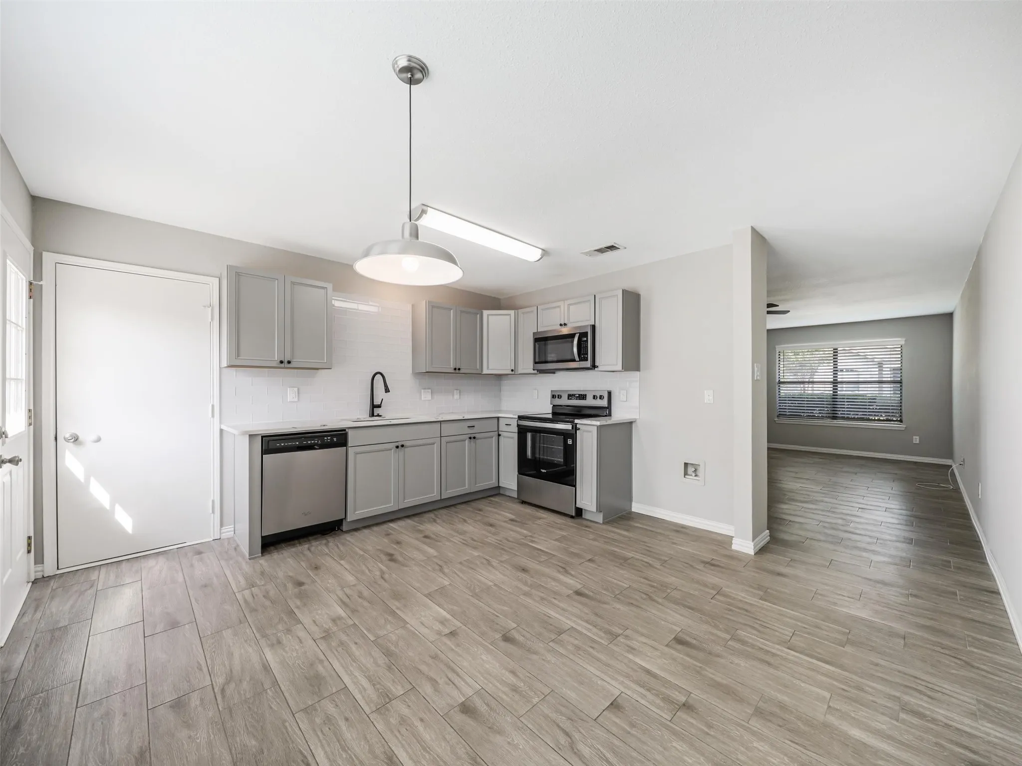 Modern kitchen featuring light gray cabinetry, stainless steel appliances, wood-finish flooring, and a white subway tile backsplash