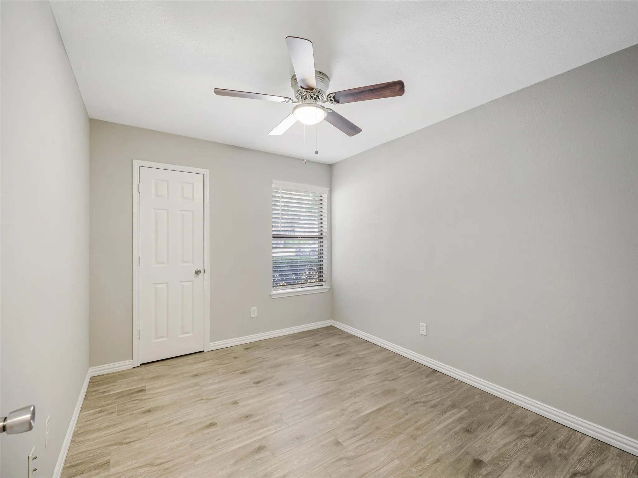 Wood-finish flooring, ceiling fan with integrated lighting, window with blinds, and a paneled door
