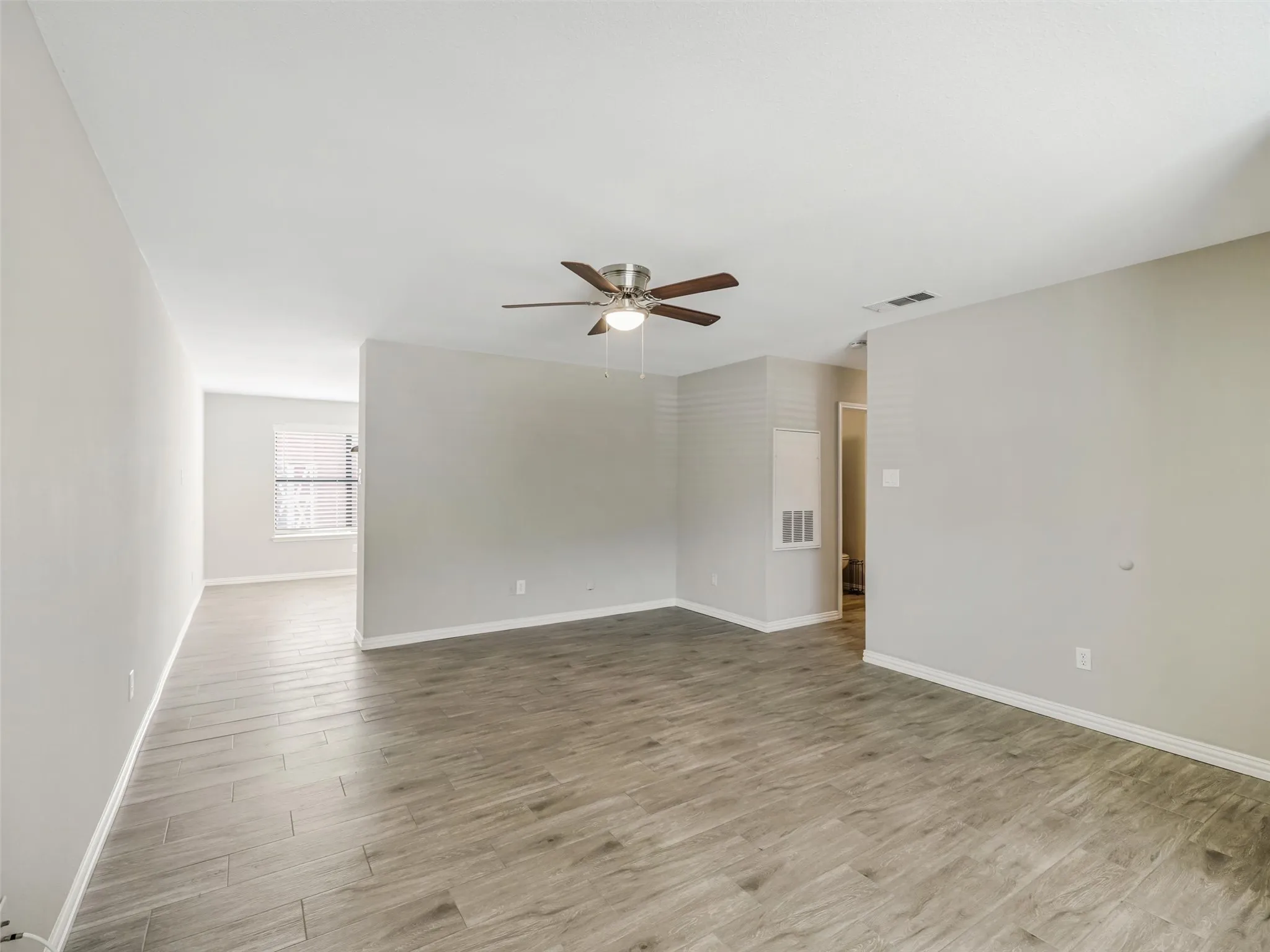 Spacious room featuring wood-look tile flooring, light-toned walls, and a ceiling fan