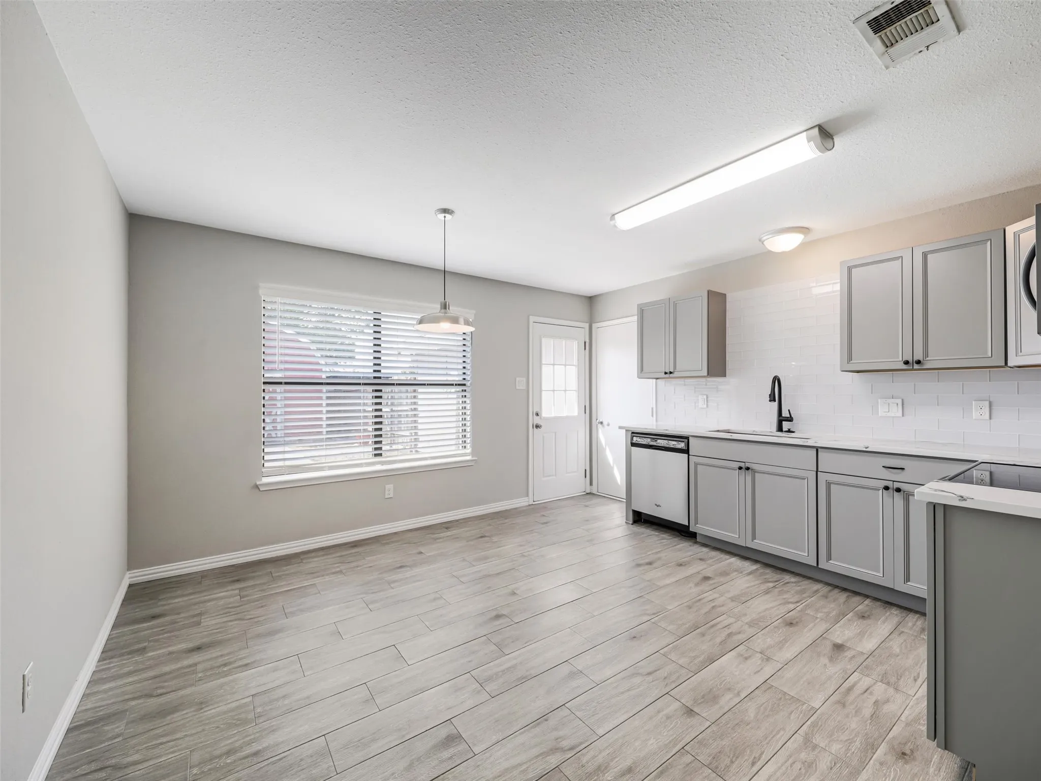 Wood-finish flooring throughout, gray cabinetry, white subway tile backsplash, white countertops, and stainless steel appliances