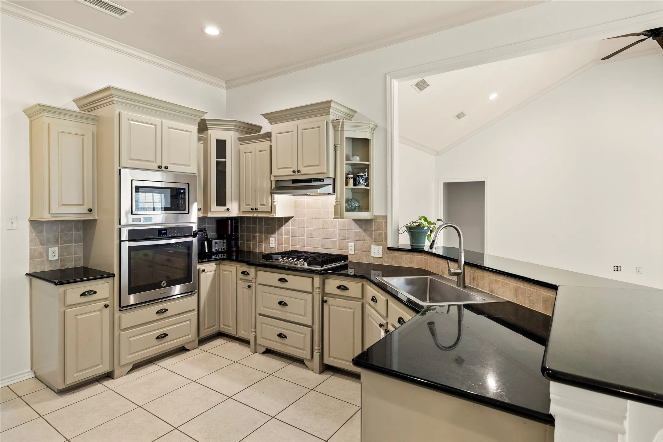 Kitchen featuring stainless steel built-in appliances, dark countertops, a tile backsplash, and light cabinetry with crown molding