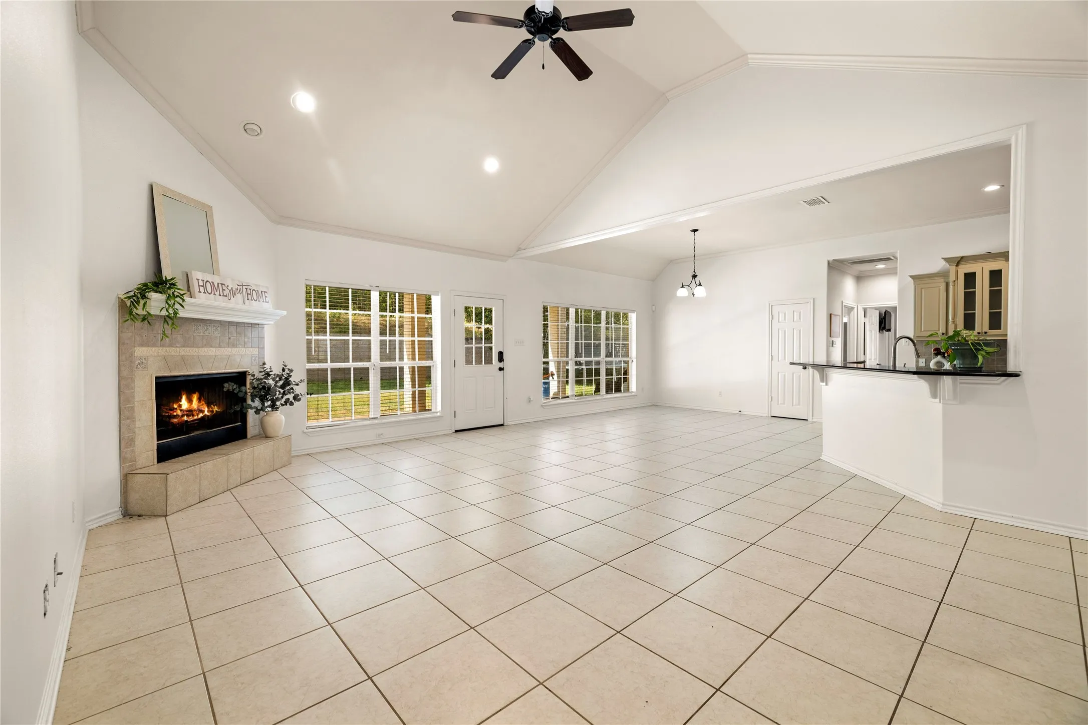 Vaulted ceiling with a ceiling fan, recessed lighting, corner fireplace with a mantel, tiled flooring, and multiple windows