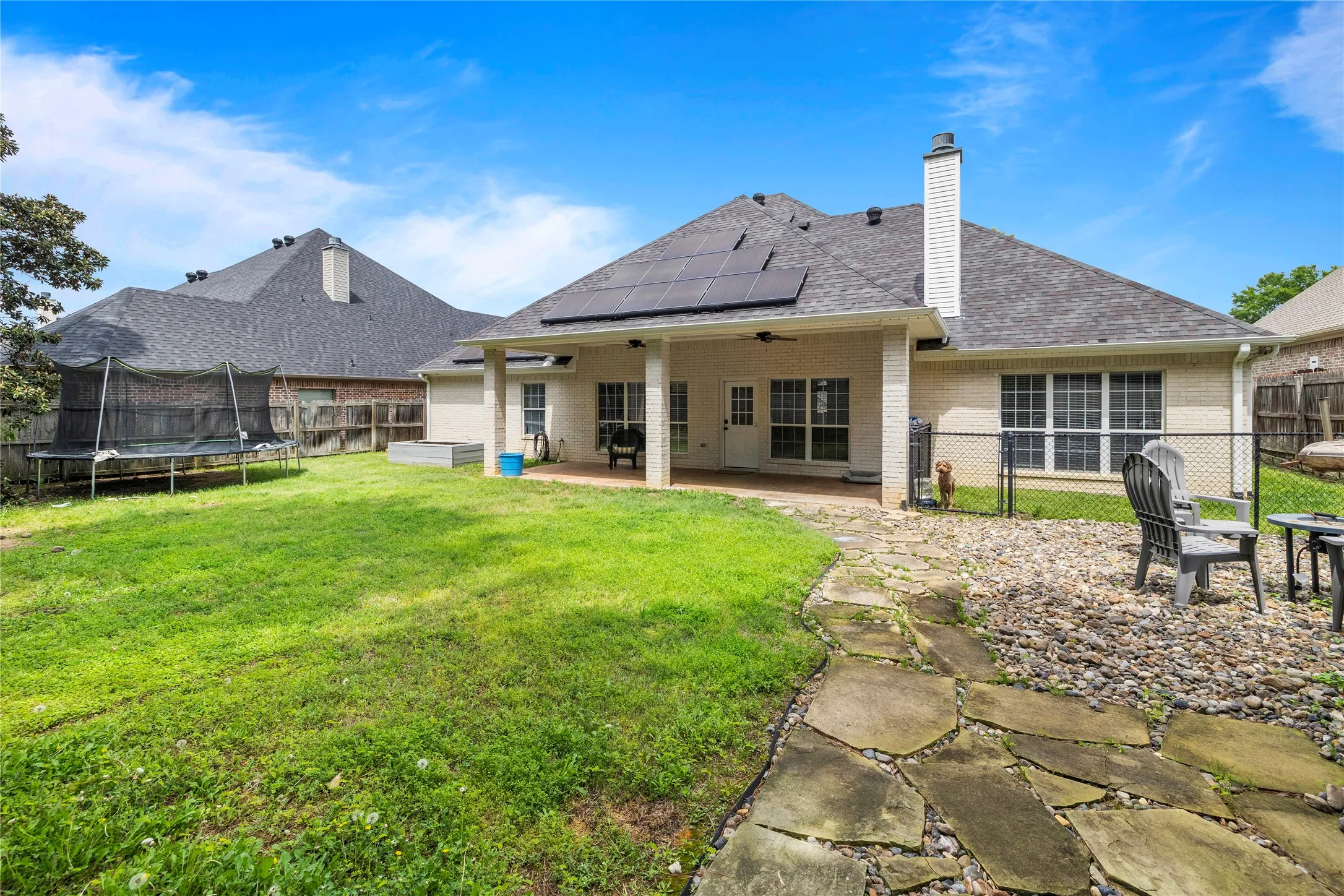 Expansive backyard featuring a covered patio, solar panels, and a stone walkway